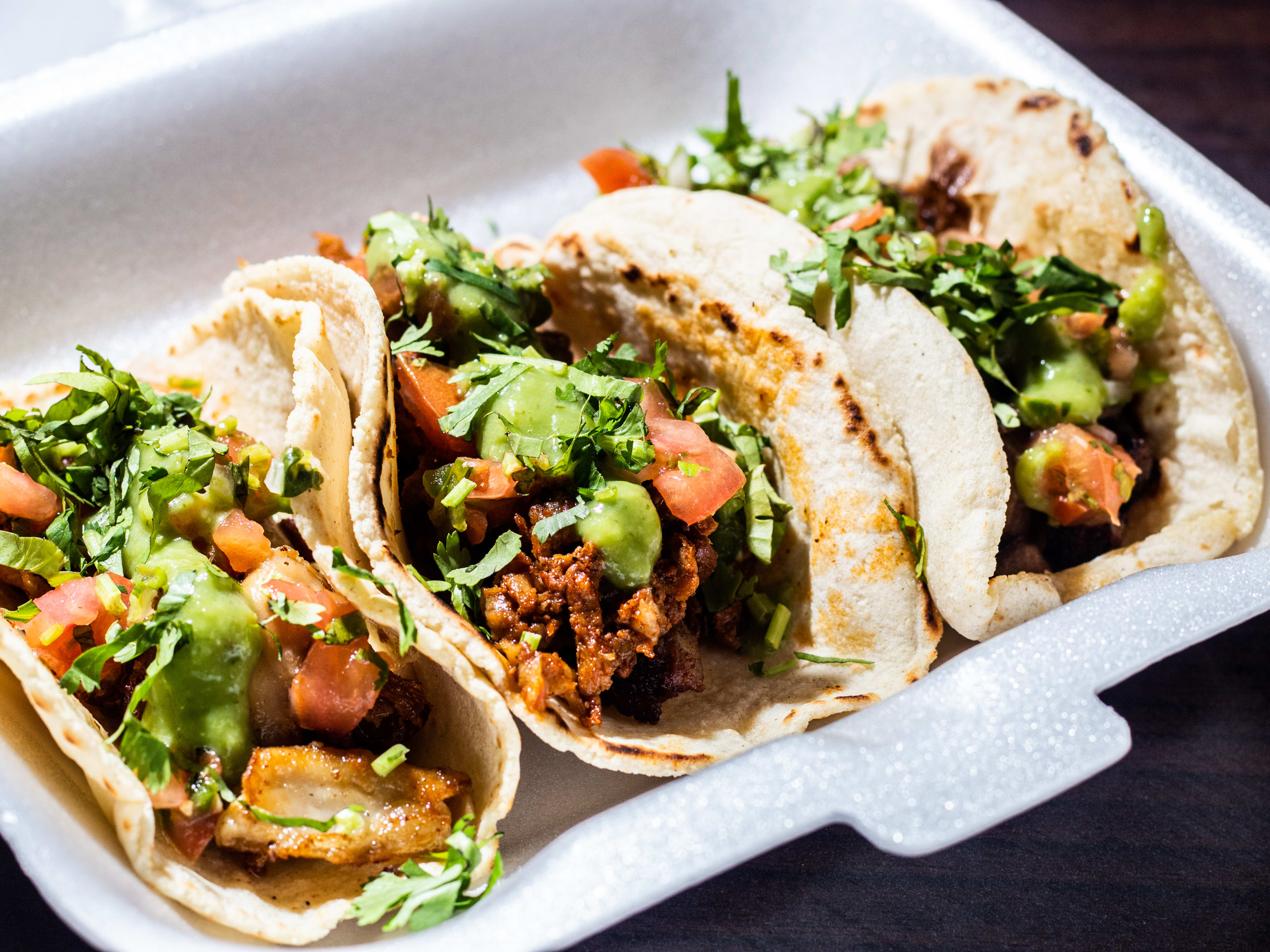 Three tripe tacos with guacamole, pico de gallo, and cilantro in a takeout box.