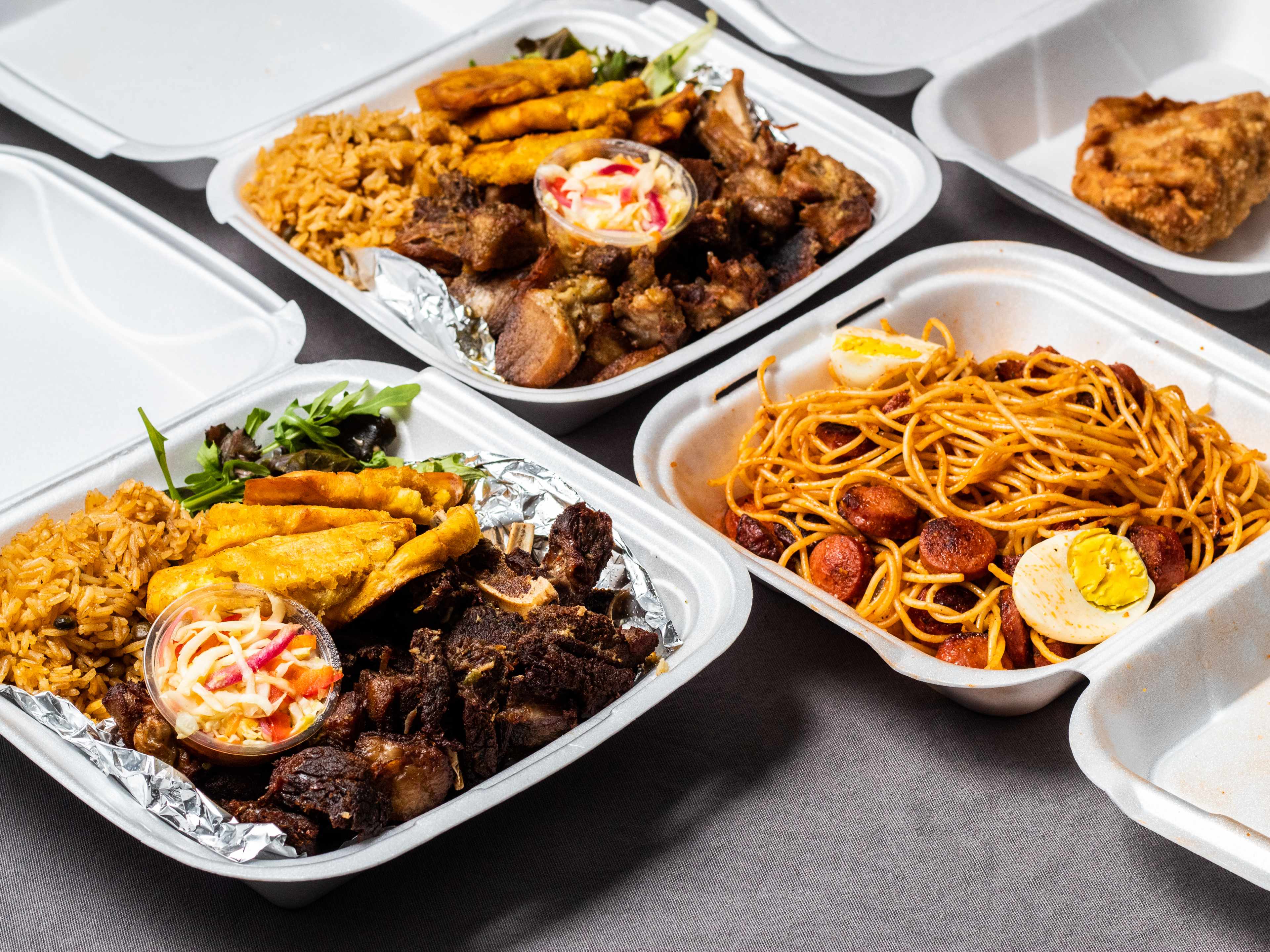 Takeout boxes full of Haitian dishes, including fried goat, spaghetti, and more.