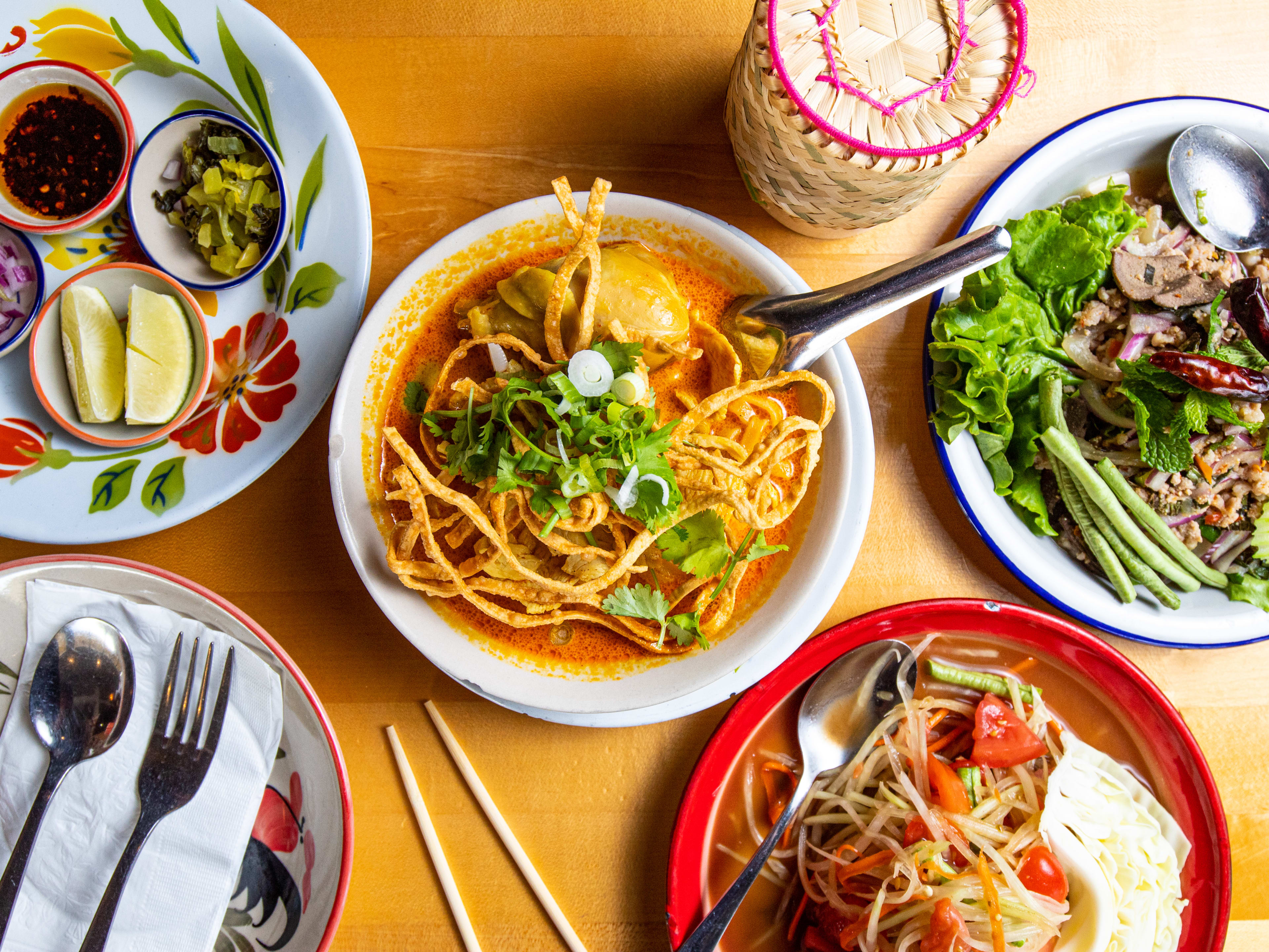 A table with several dishes of Thai food, including a khao soi in the middle.