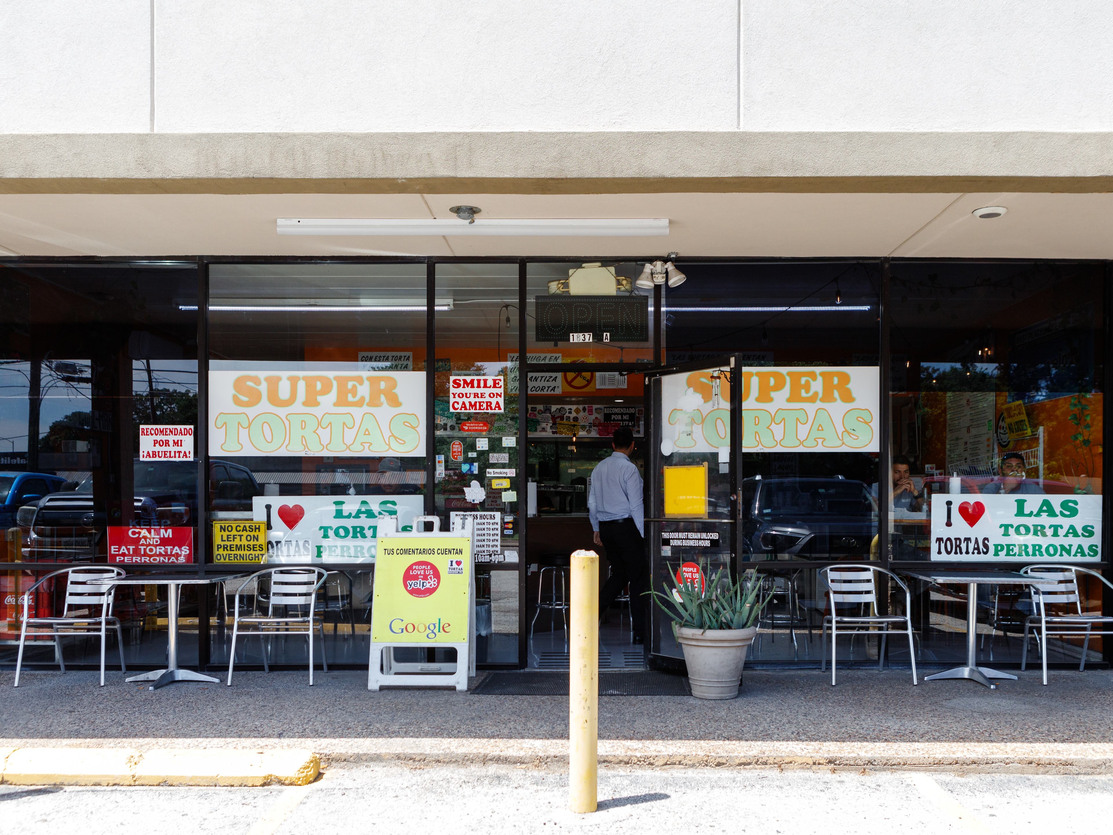 exterior of Tortas Las Perronas located in a strip center with multiple photos and signs in the window