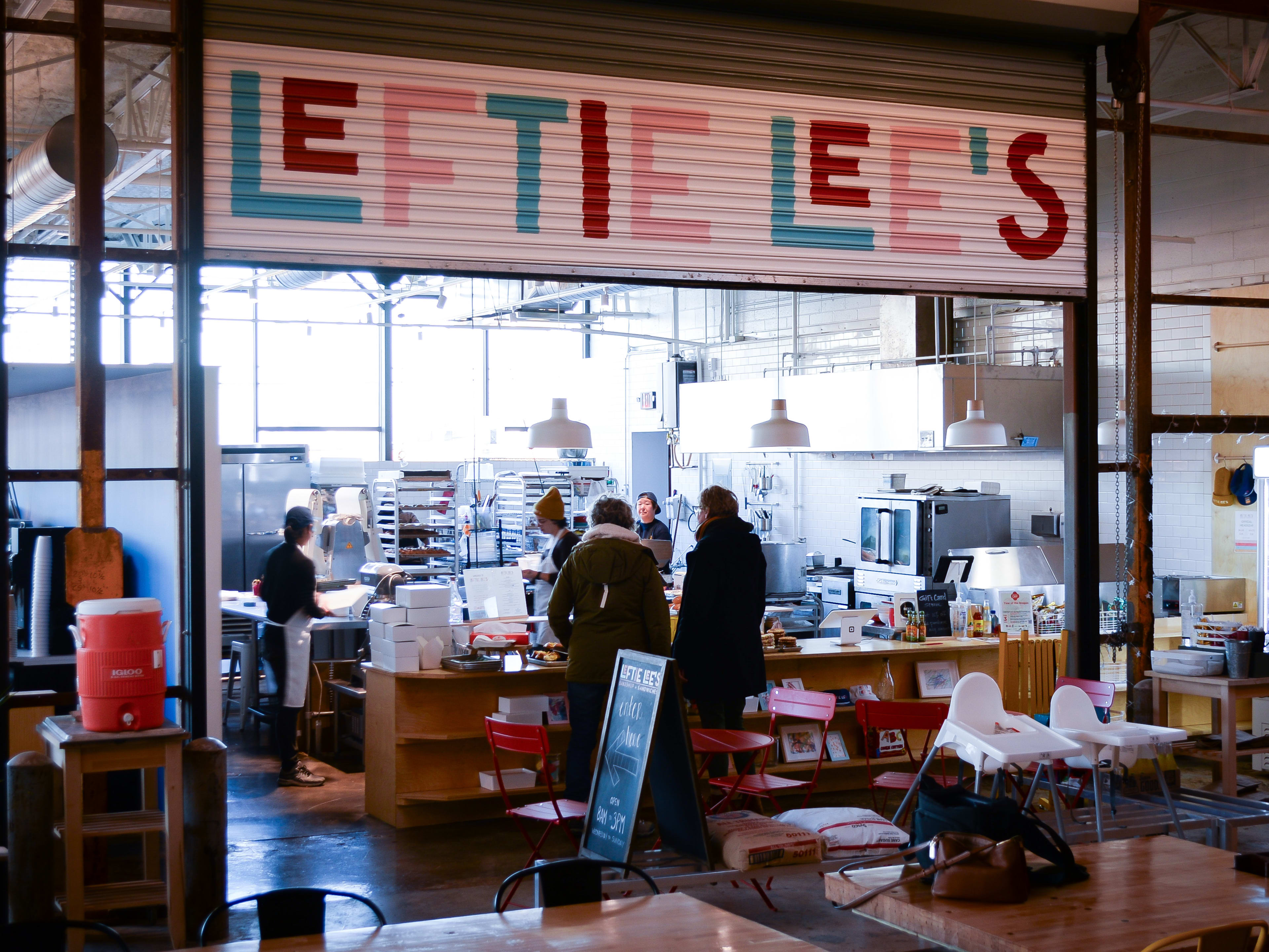 Interior of food hall bakery with colorful sign and ordering counter with bakery production visible in back.