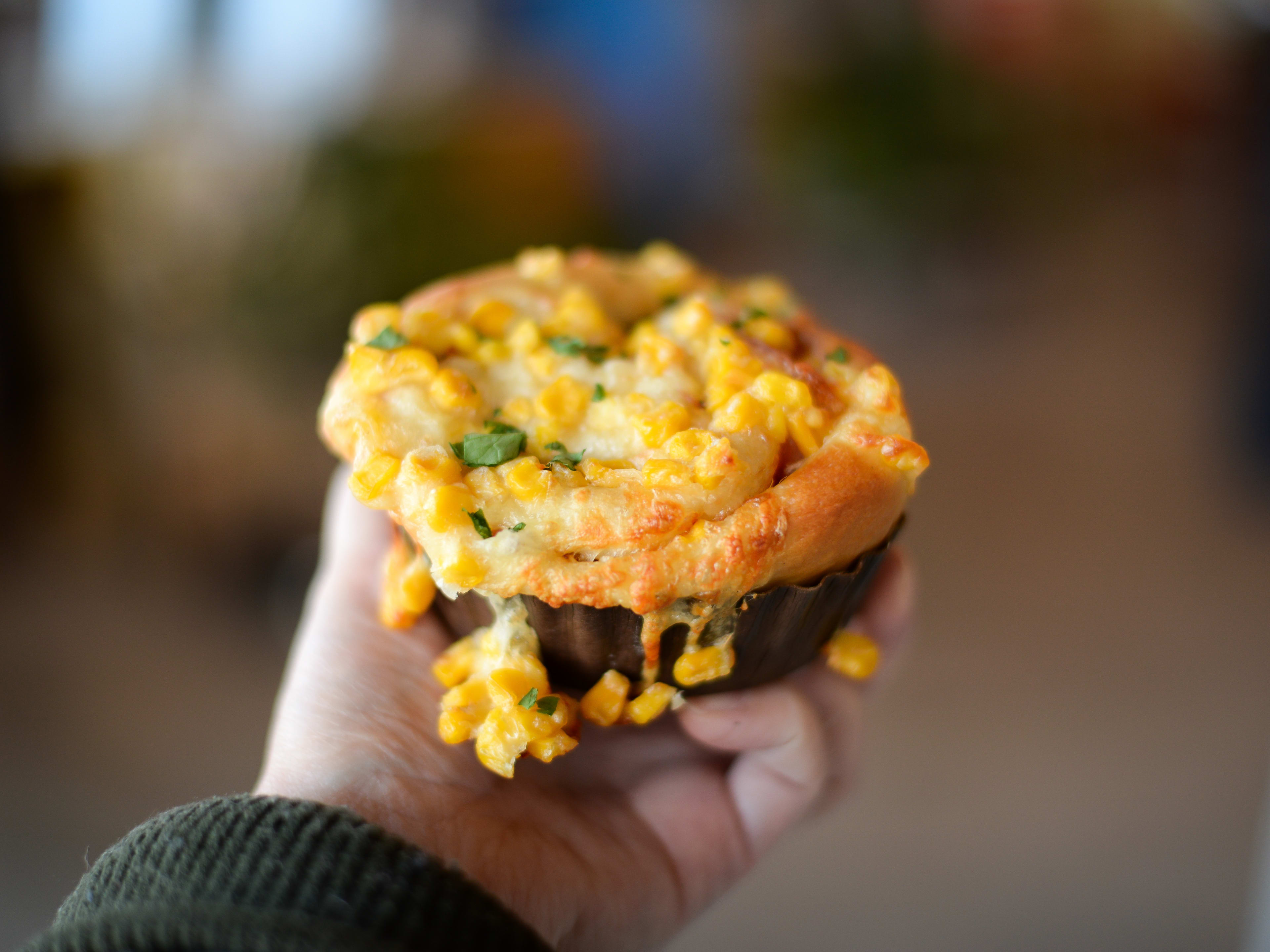 Hand holding bread bun topped with corn and melty cheese.