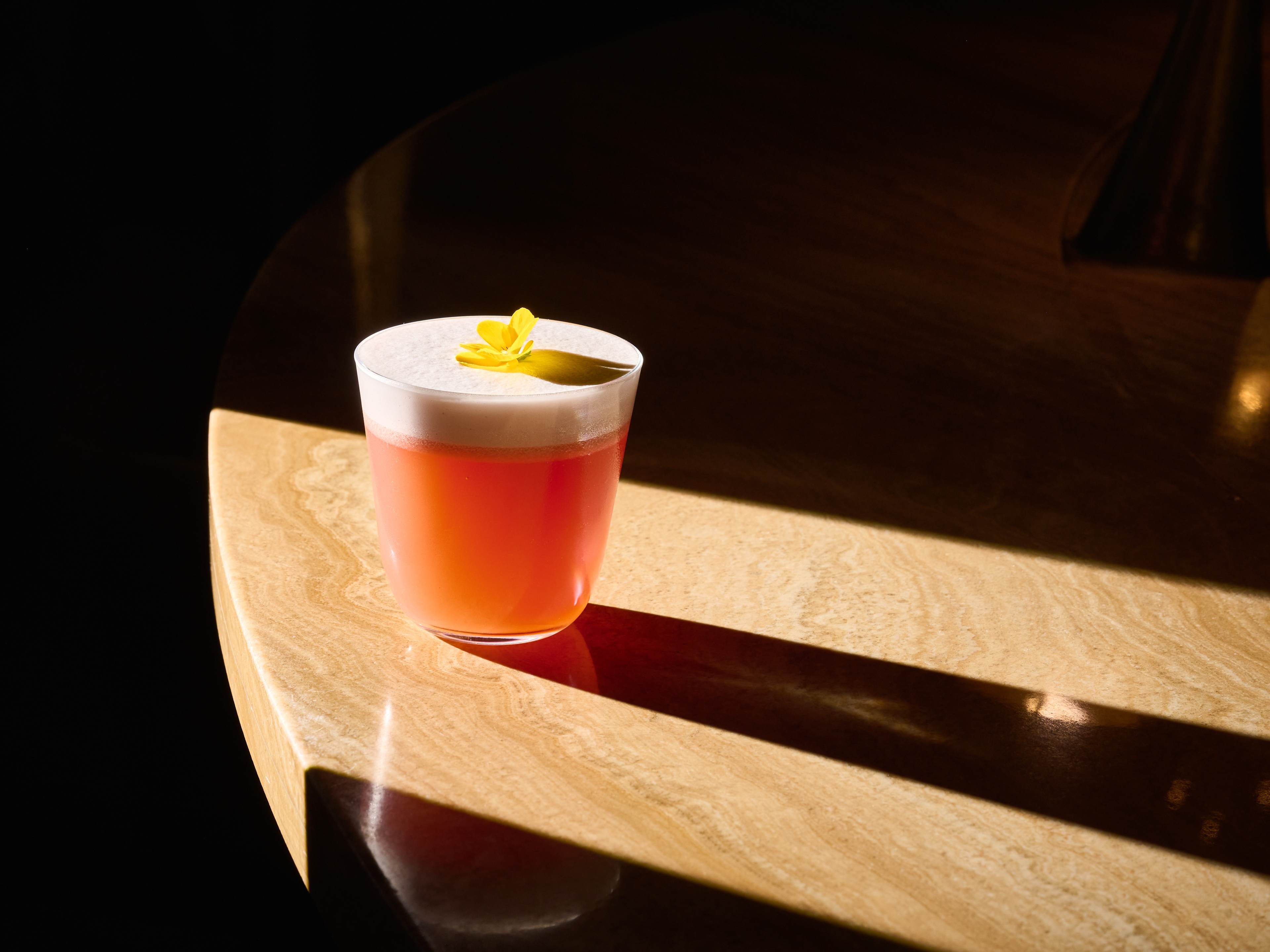 Pink cocktail with egg white foam and topped with edible flower garnish at Bar Les Ambassadeurs