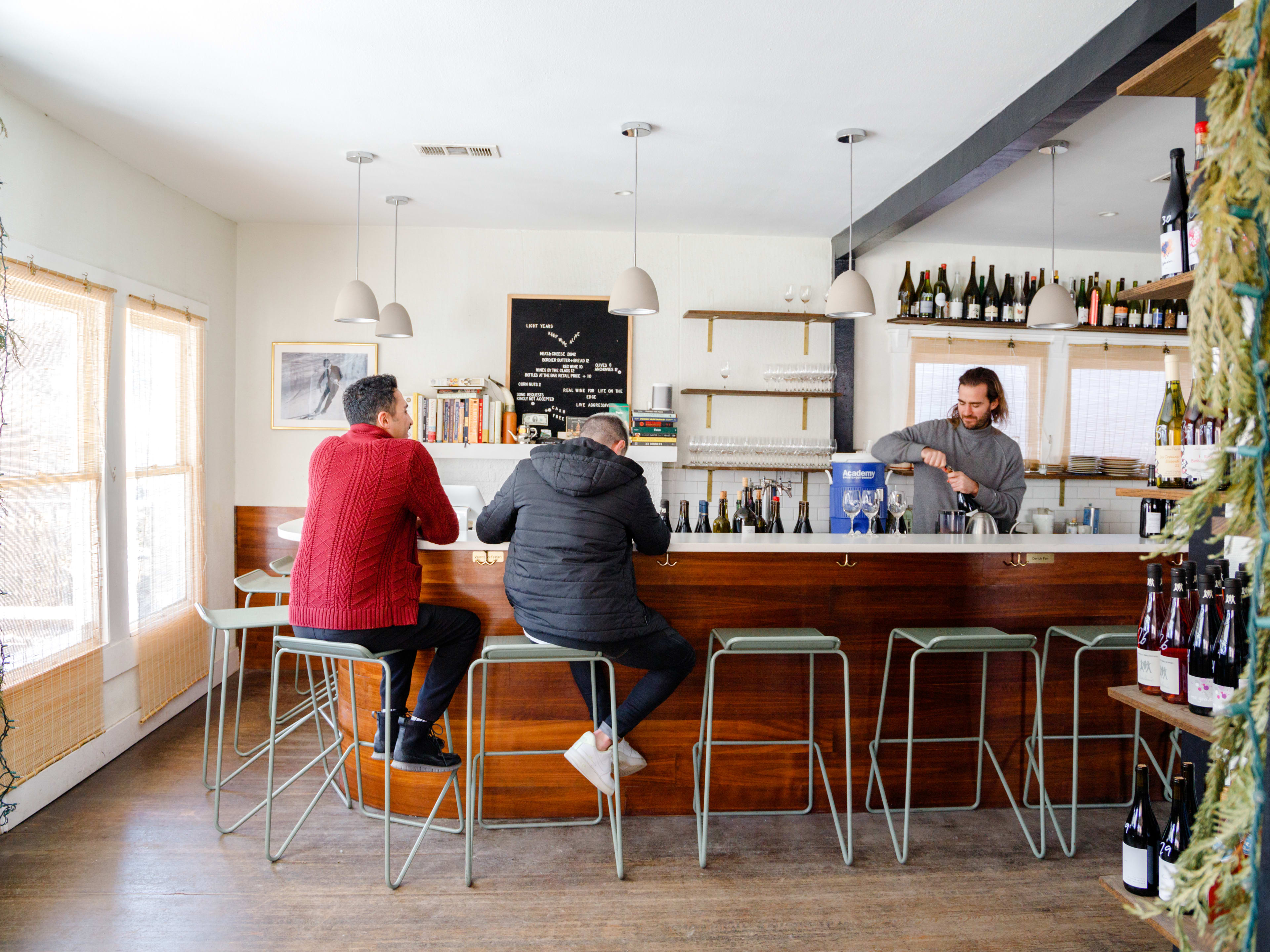 Two people sit at the bar at Light Years while a bartender opens a wine bottle.