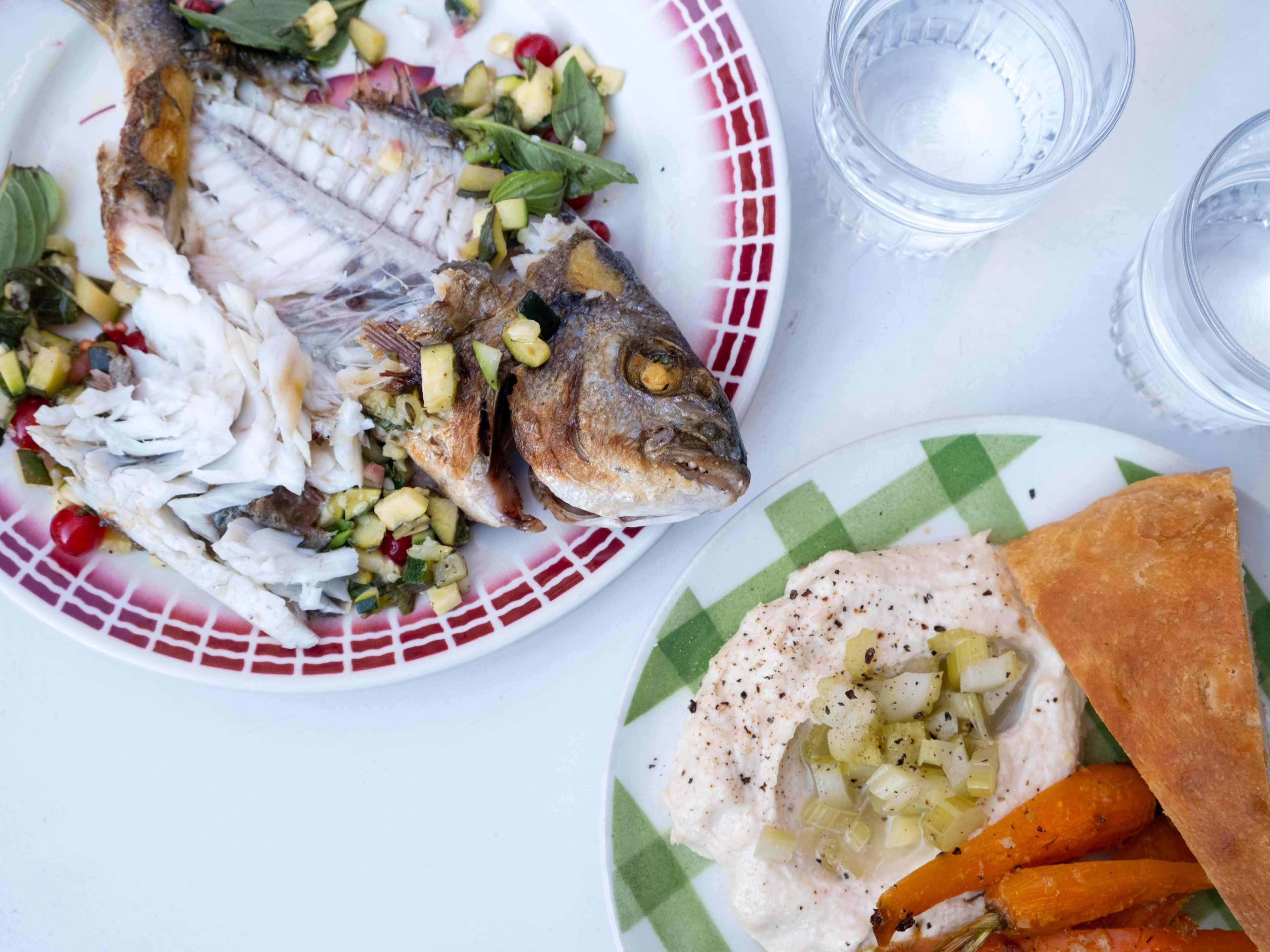 A plate of fish on the bone and another appetizer on plates, on a table