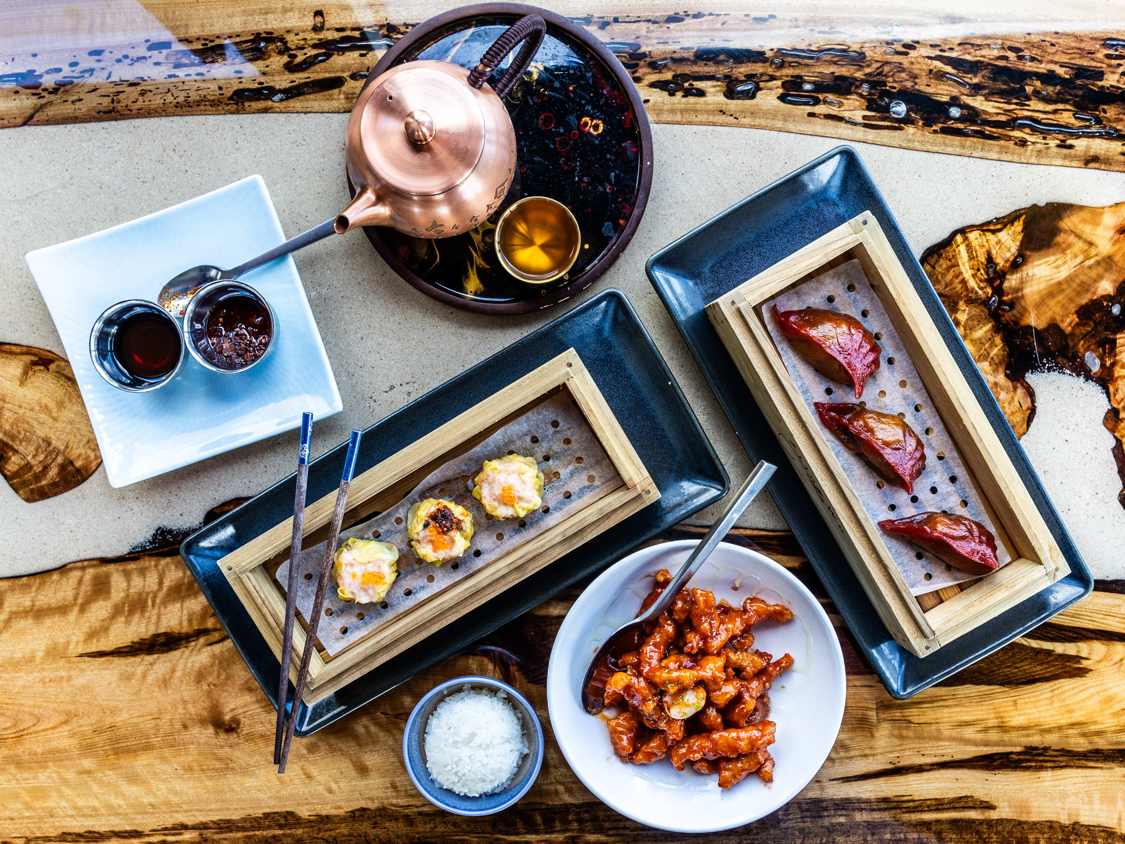 A group of various dishes from King Wu on a cream epoxy resin wooden counter.