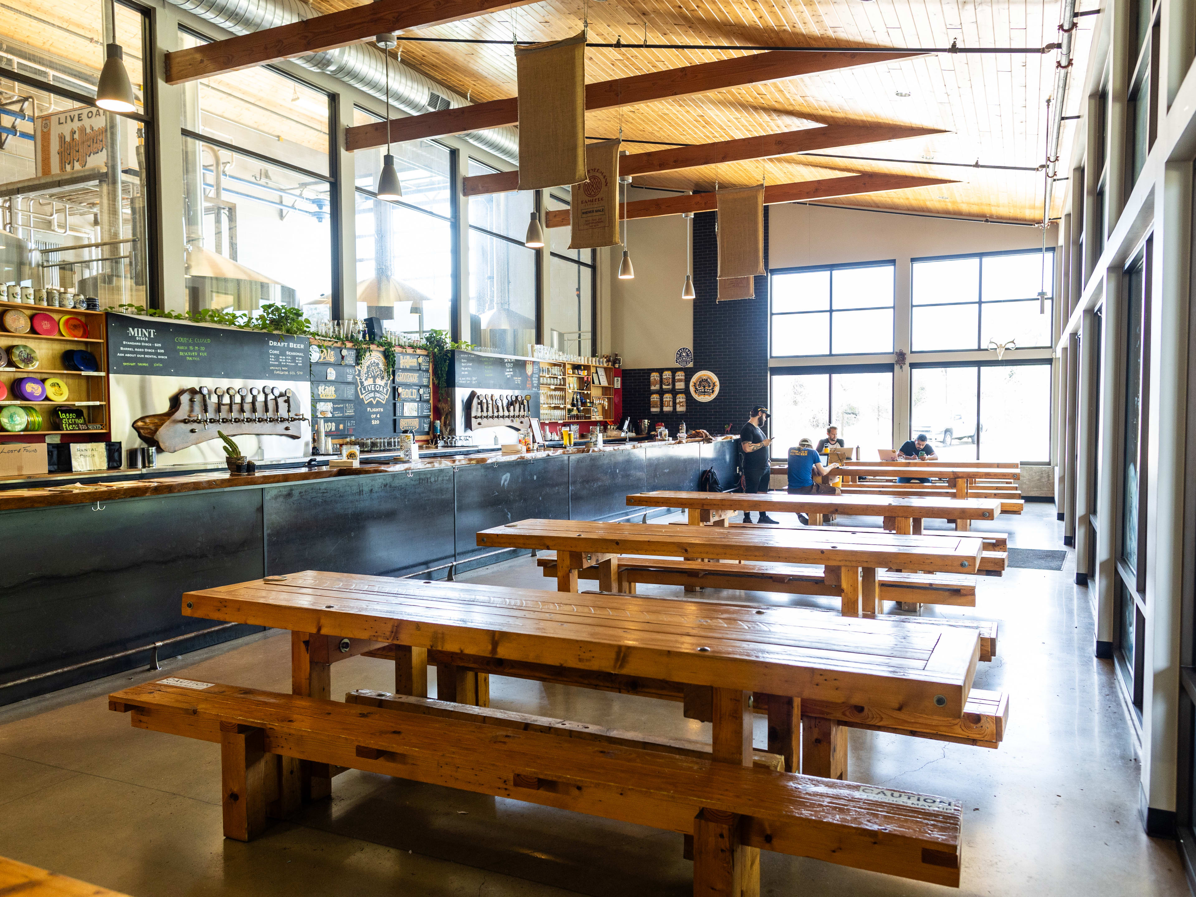 The spacious interior of Live Oak lined with wooden picnic style tables, and a long bar.