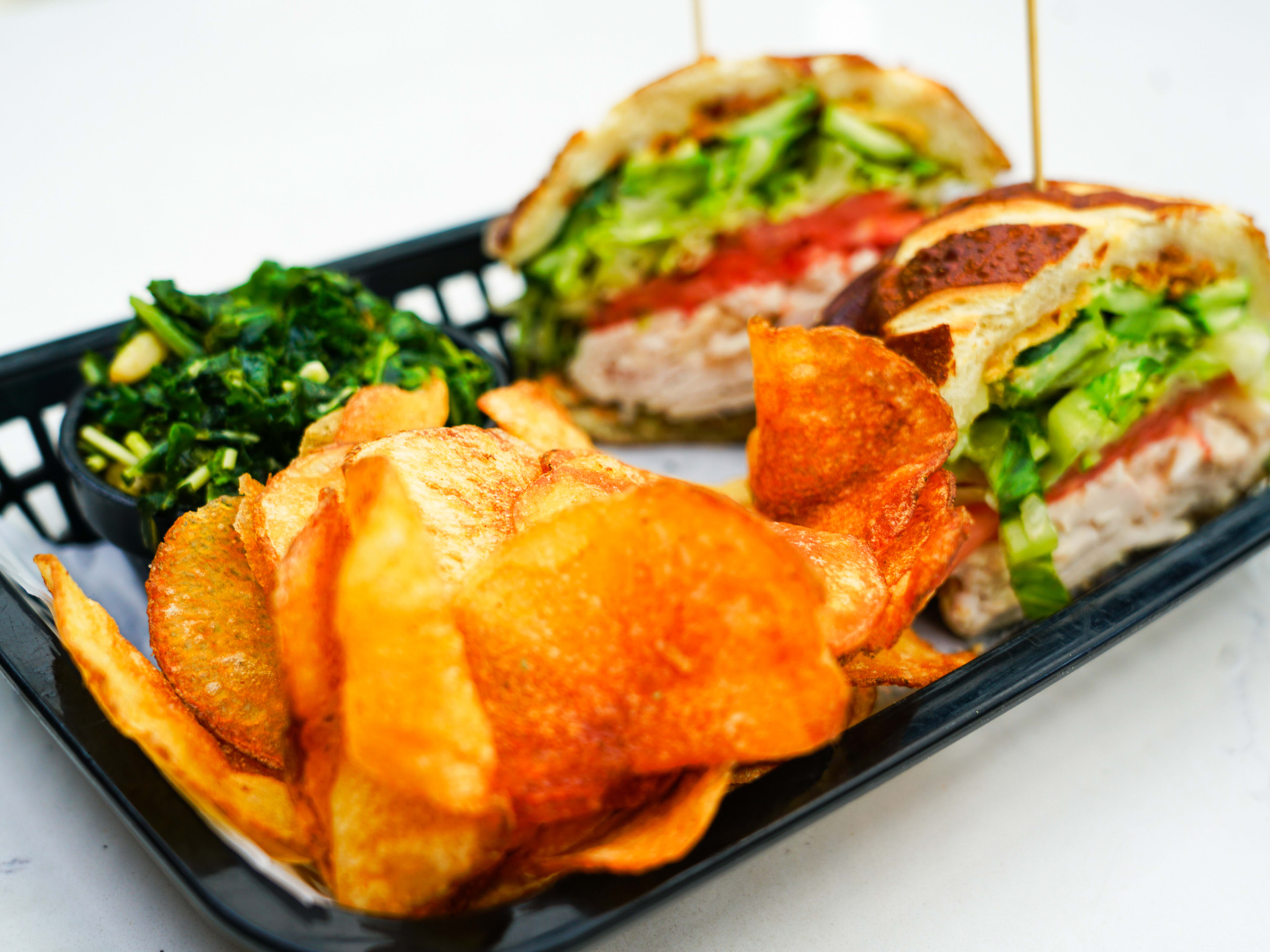 photo of chicken sandwich topped with lettuce and a side of potato chips