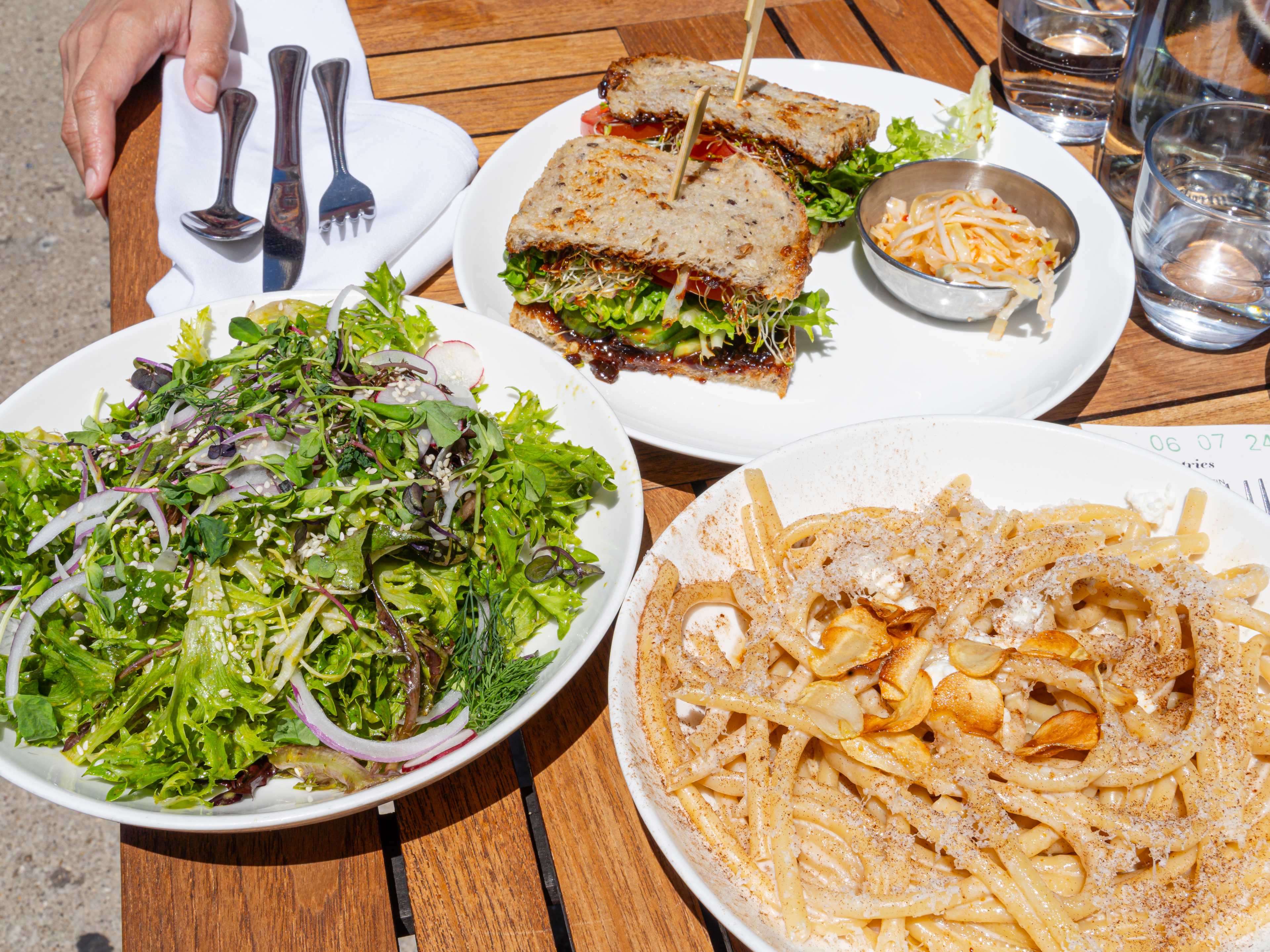 A sandwich, salad and pasta dish on a table on the patio at Lula Cafe.