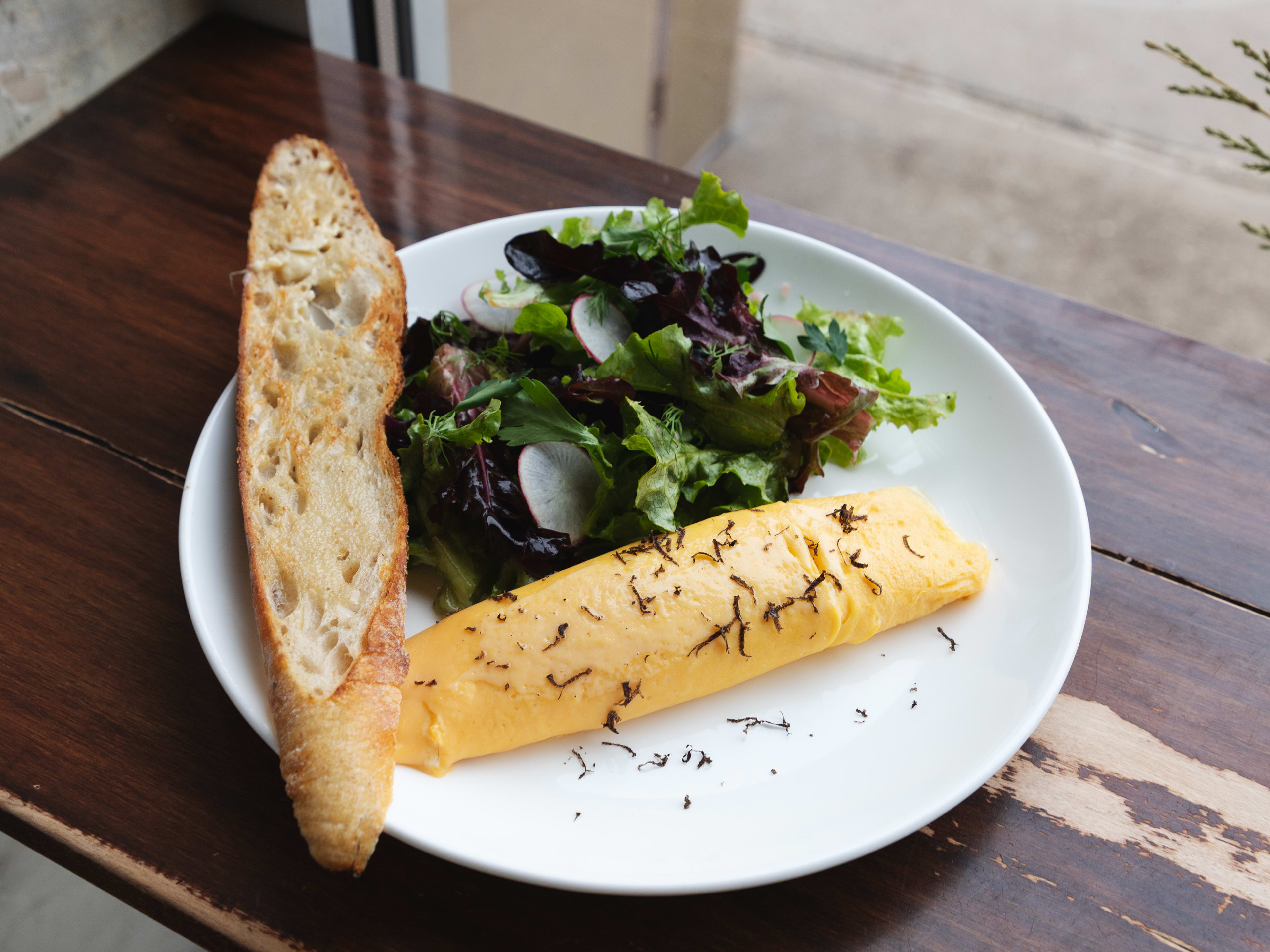 An omelet, a salad, and a piece of bread on a plate sitting in a windowsill.