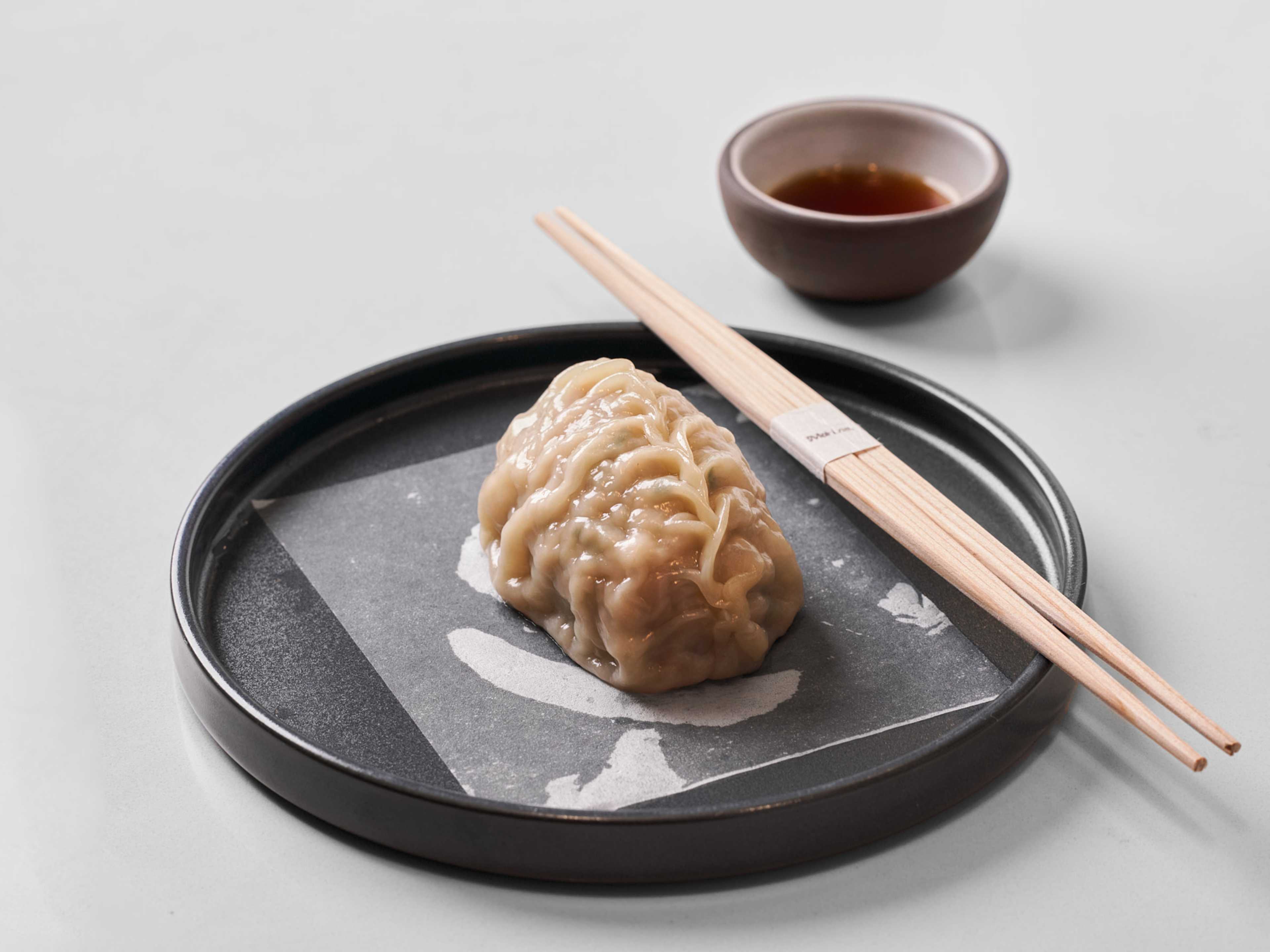 A big dumpling on a plate with chopsticks on the side.