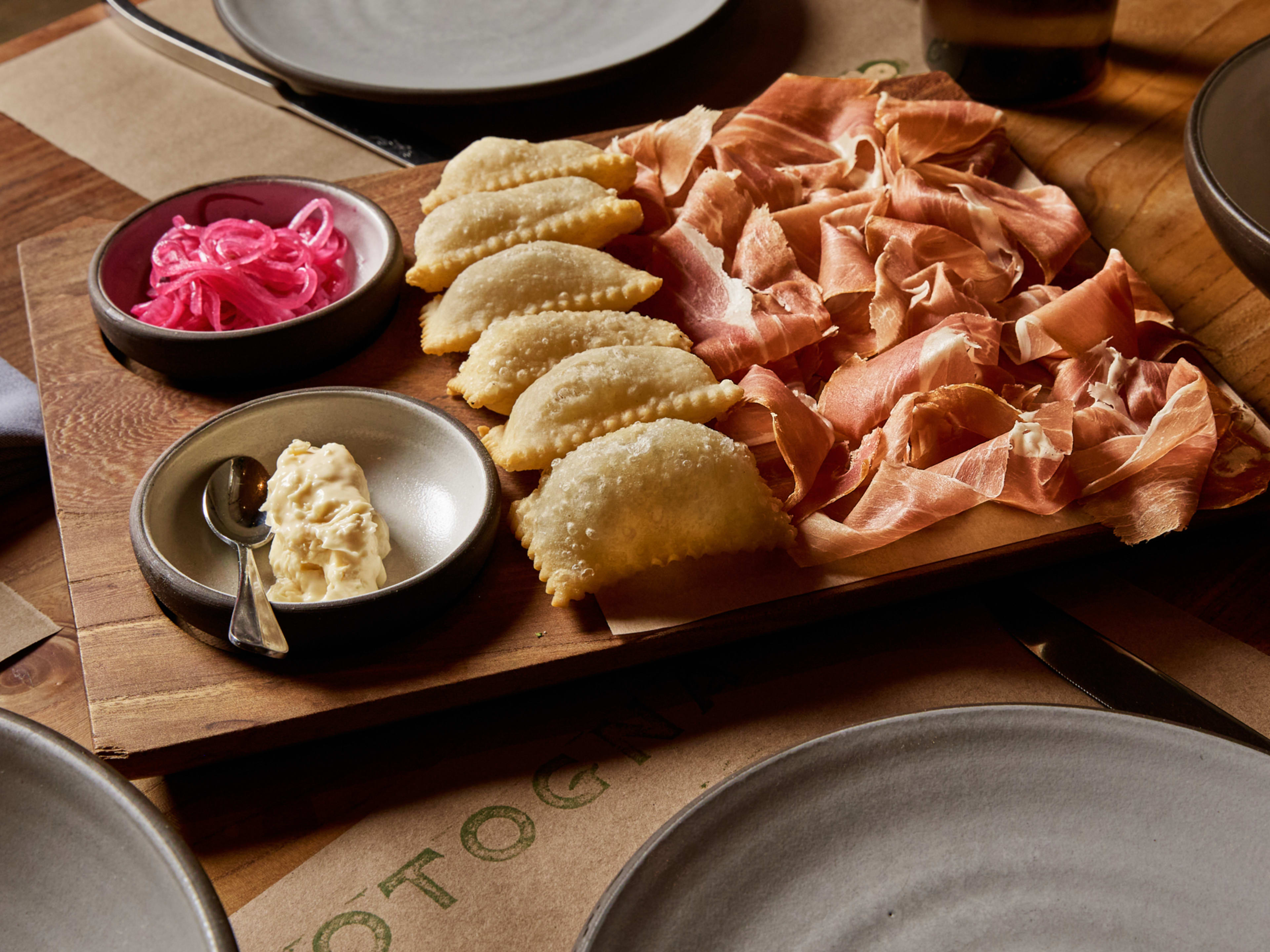 wooden board with prosciutto, gnoccho fritto, pickled onions, and butter in little dishes.