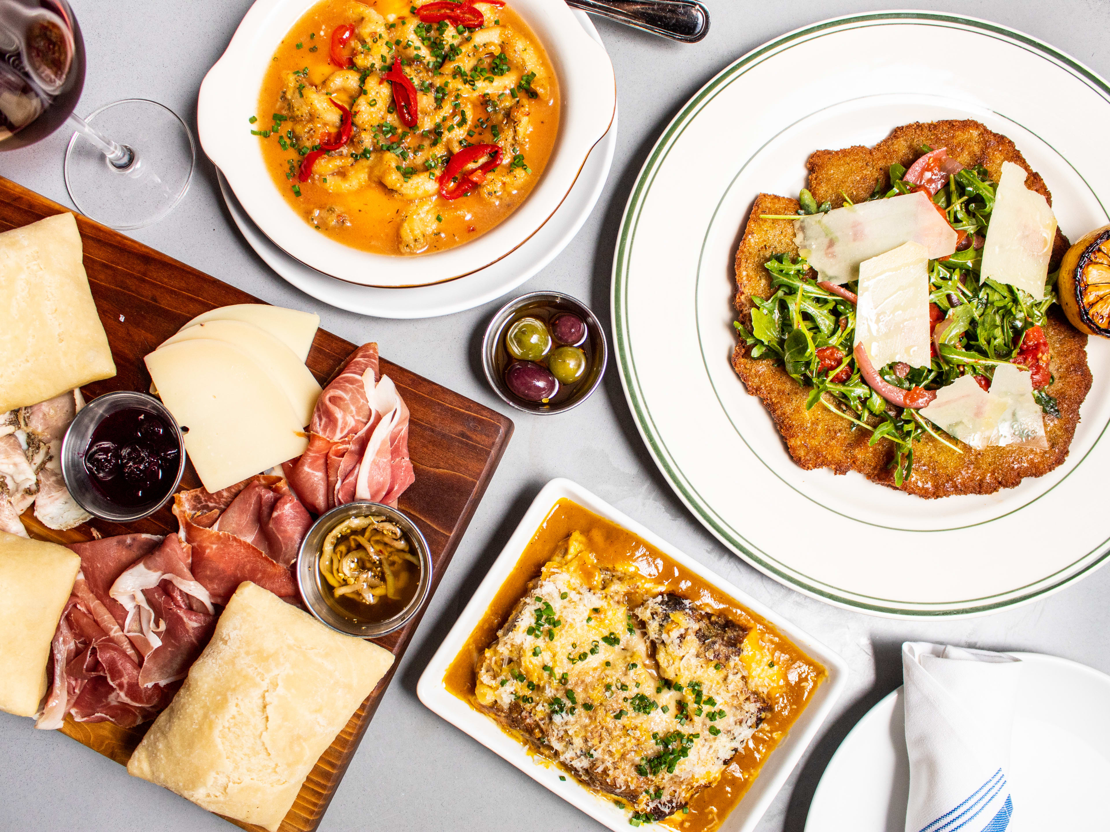 Spread of dishes including cutlet, soup, pasta, and charcuterie board with meats and cheeses.