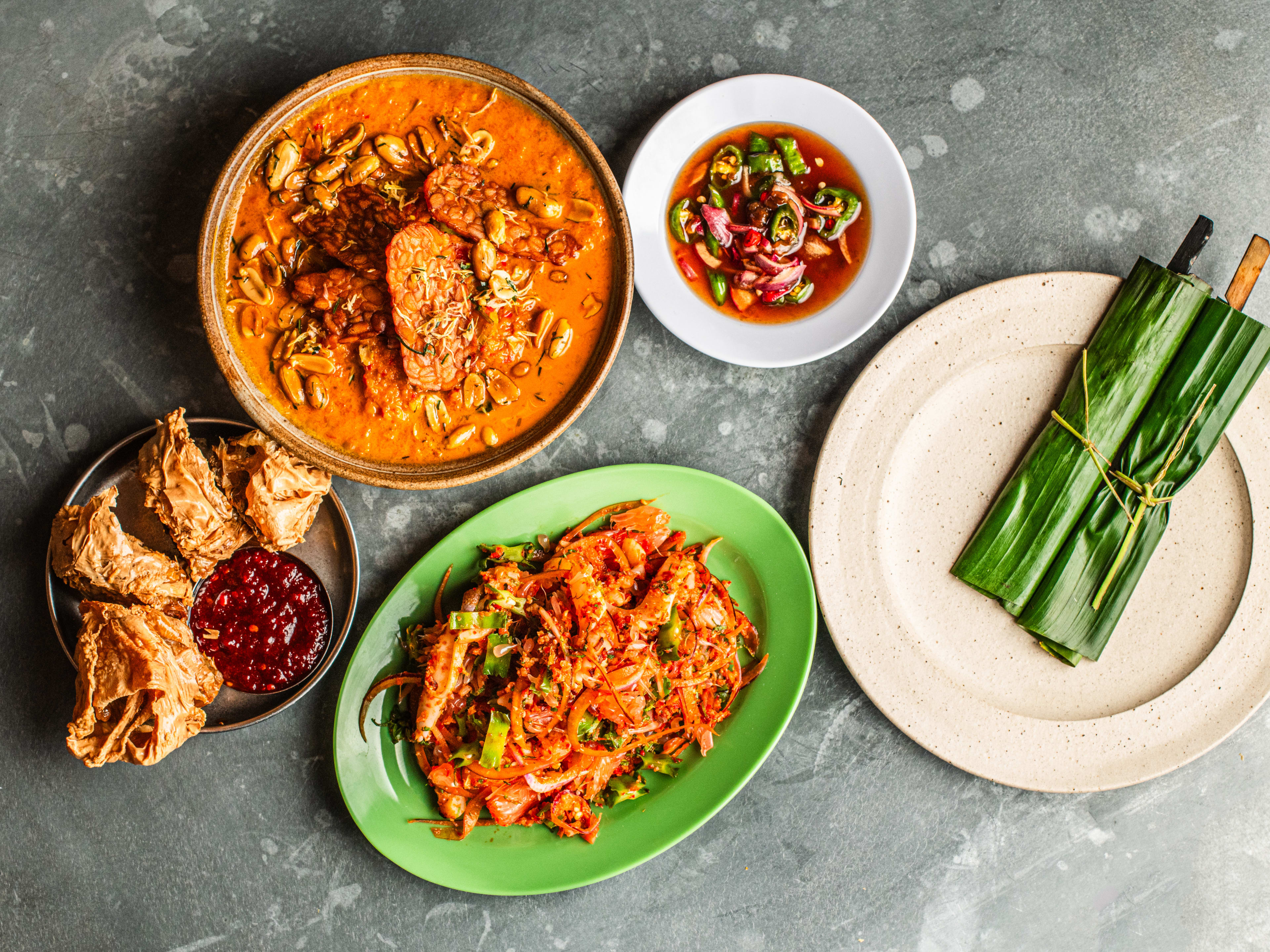 An overhead shot of curry, chicken skewers, lor bak, and cuttlefish salad from Mambow.