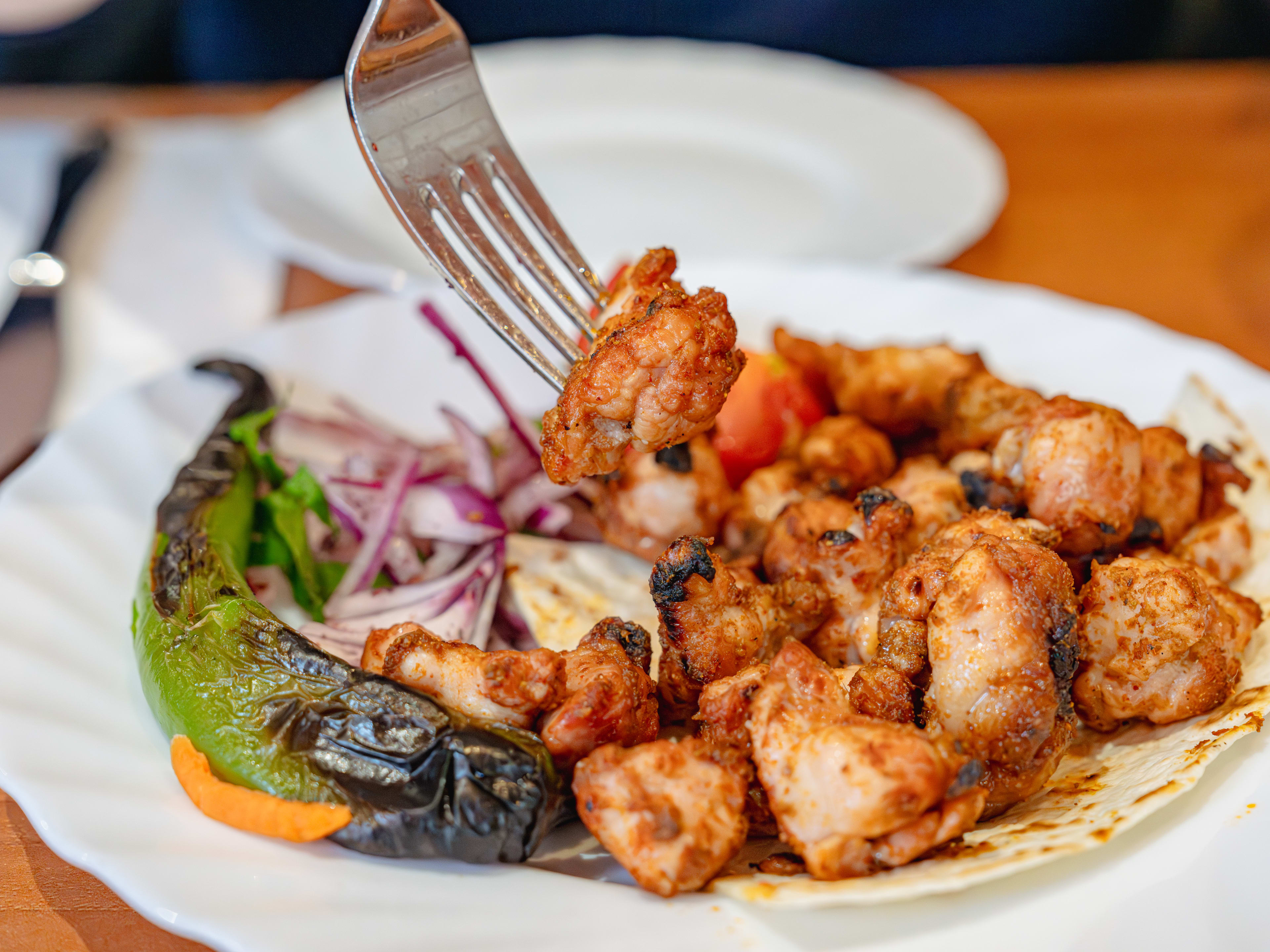 A fork digs into a white plate of sweetbreads and a large green pepper from Mangal 1.