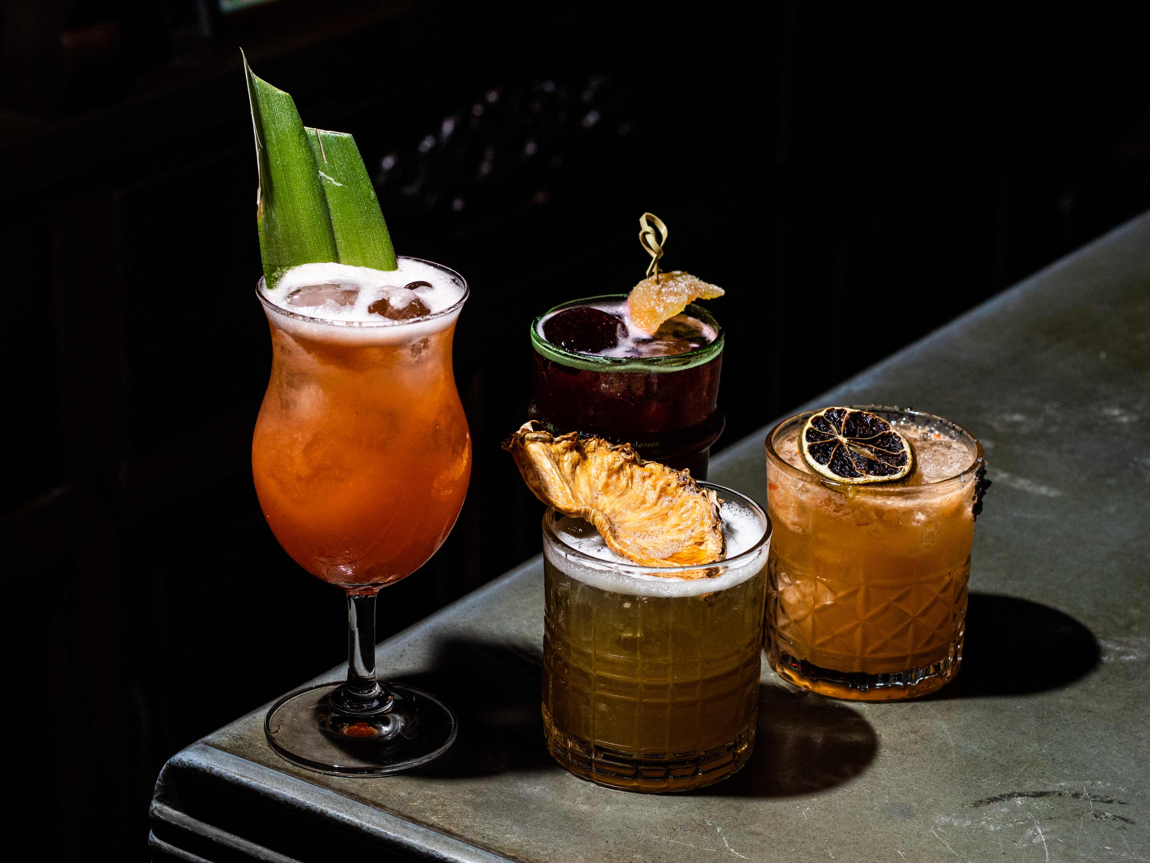 Four cocktails garnished with different fruits.