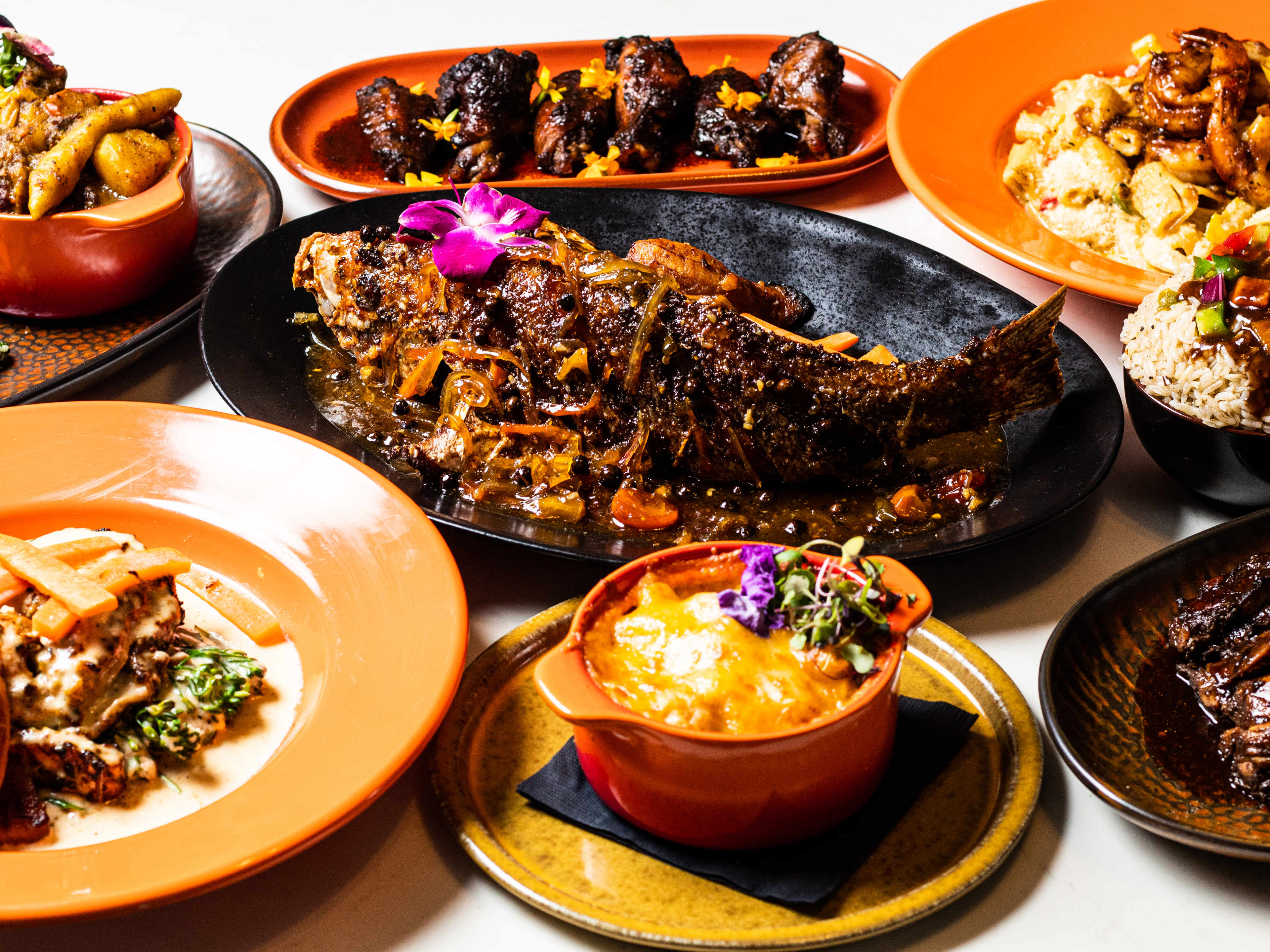 Series of Caribbean dishes garnished with flowers including a whole fried snapper in the middle.