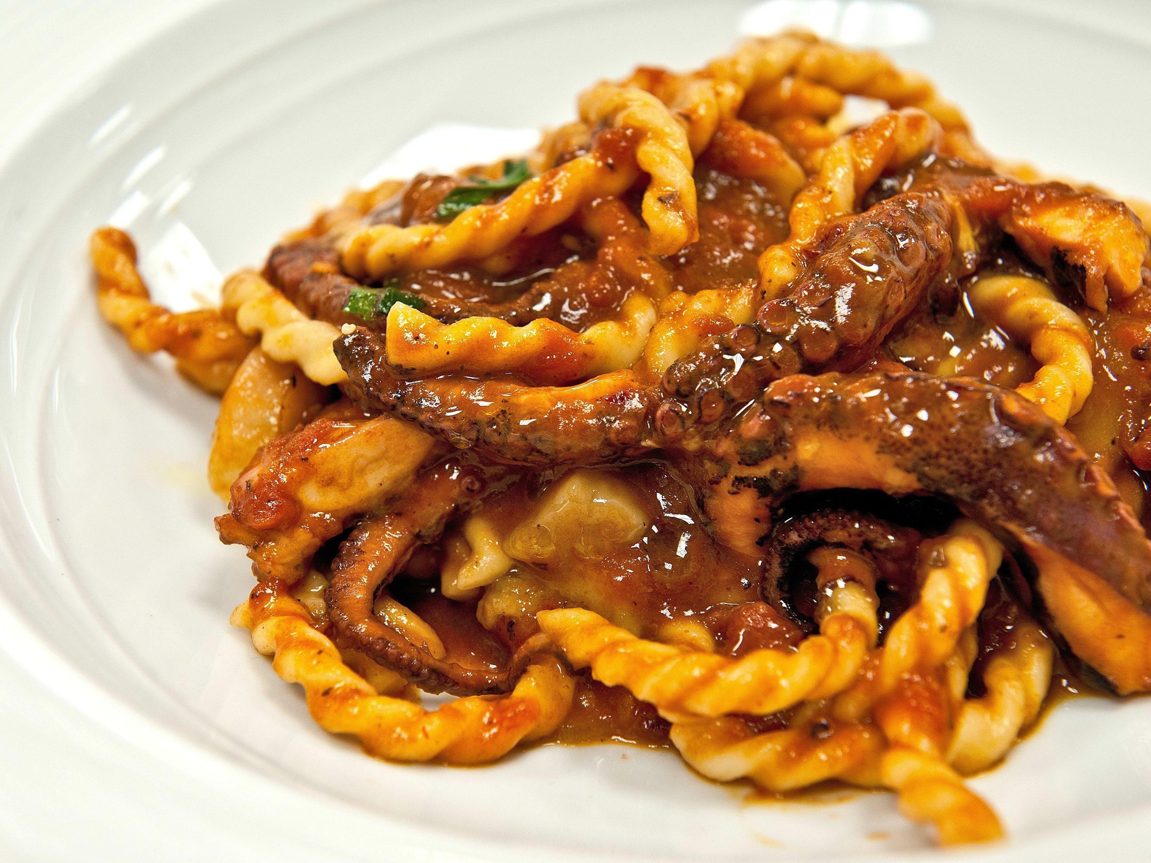 A bowl of fusilli with a thick sauce and pieces of octopus.