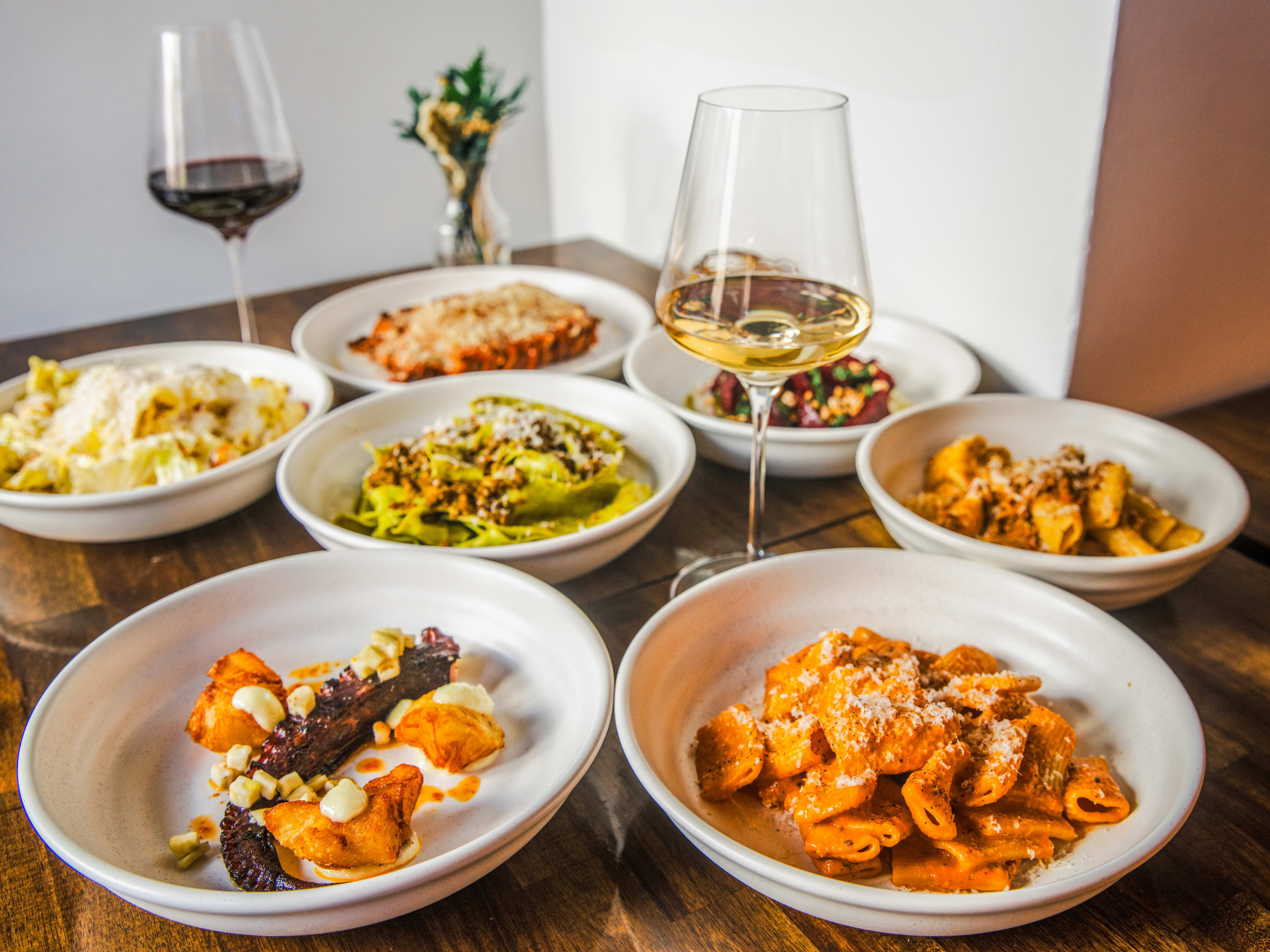 A few bowls of pasta on a table with a couple of glasses of wine.