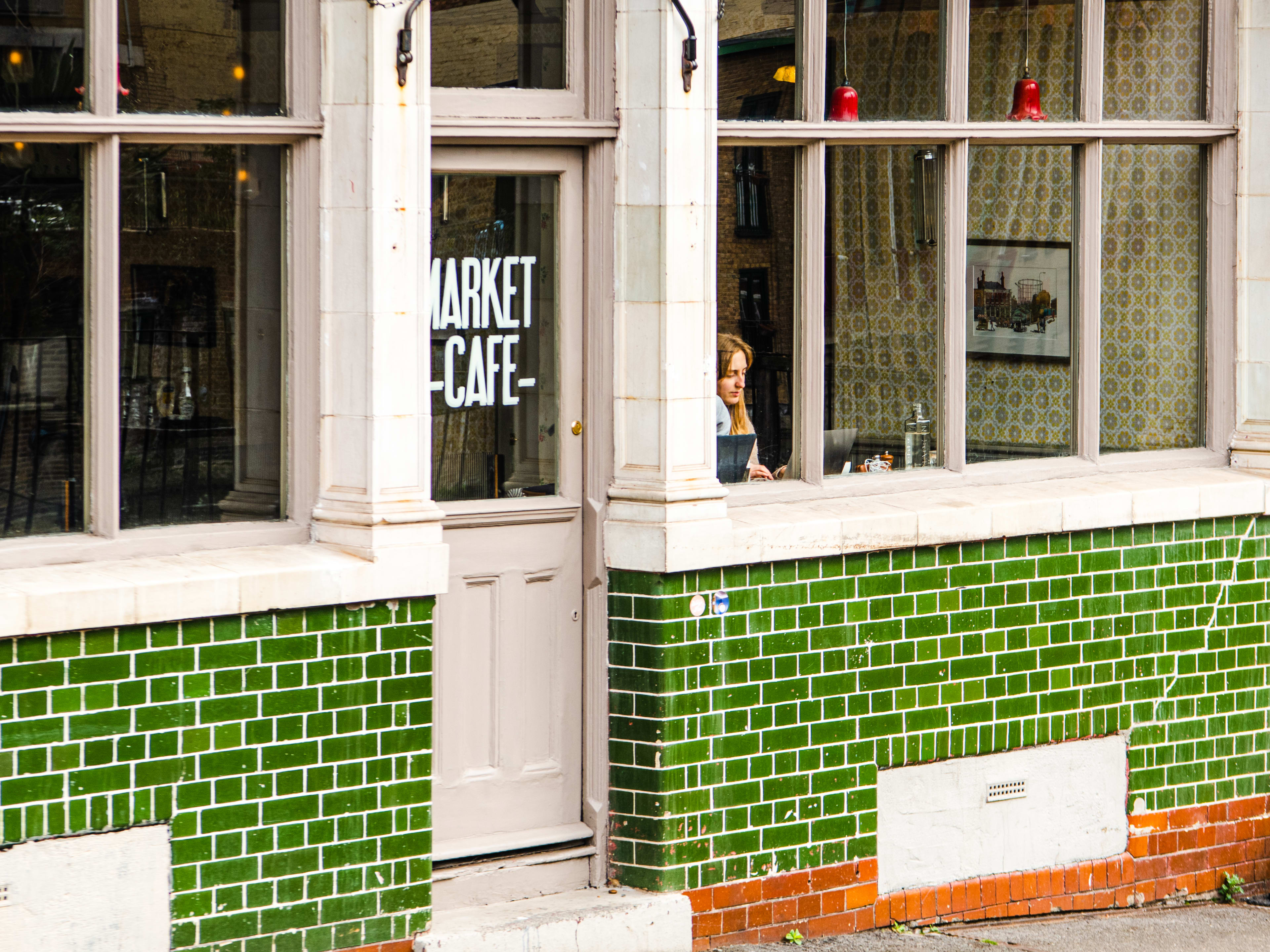 The green tiled exterior of Market Cafe. A person is seen working on their laptop at the window counter.