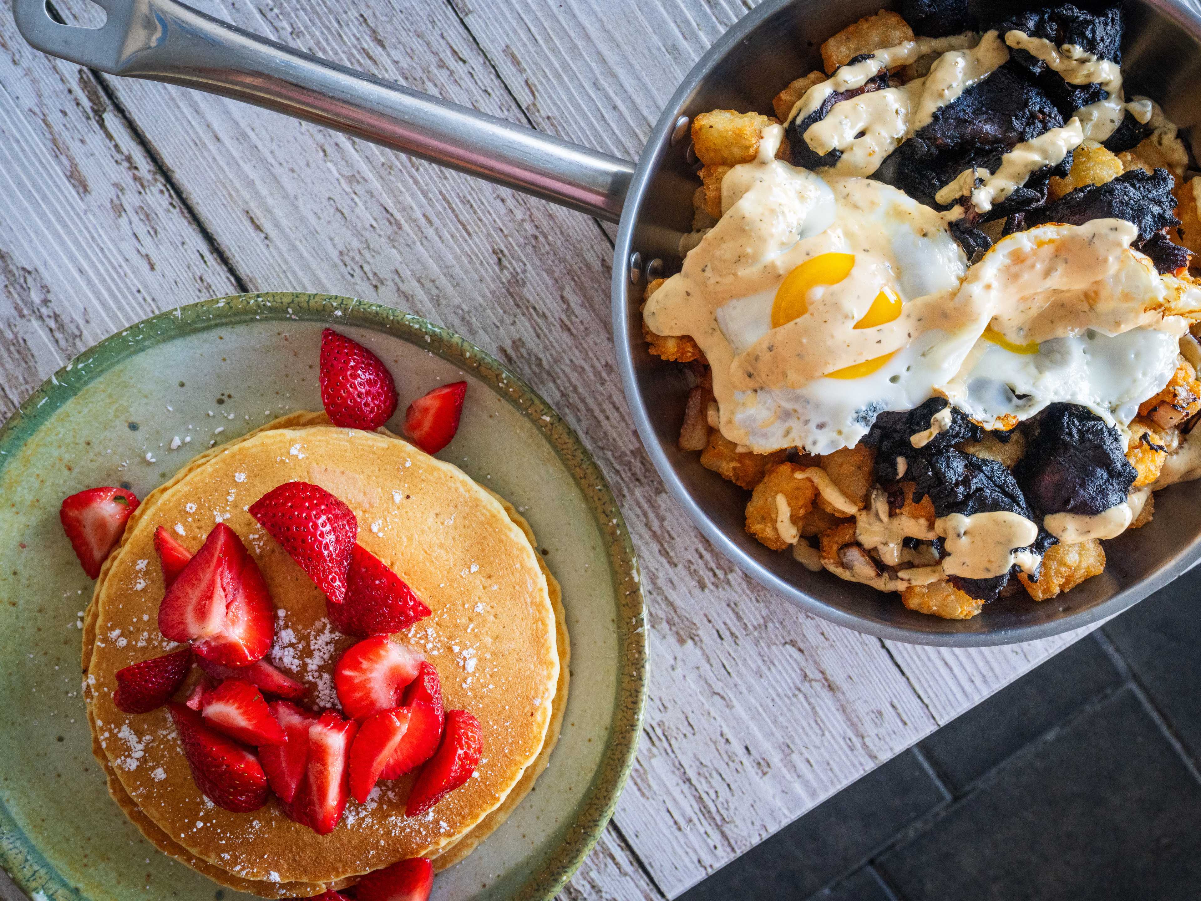 Spread of food on a wood table including the Southern Skillet and buttermilk pancakes with fresh strawberries.