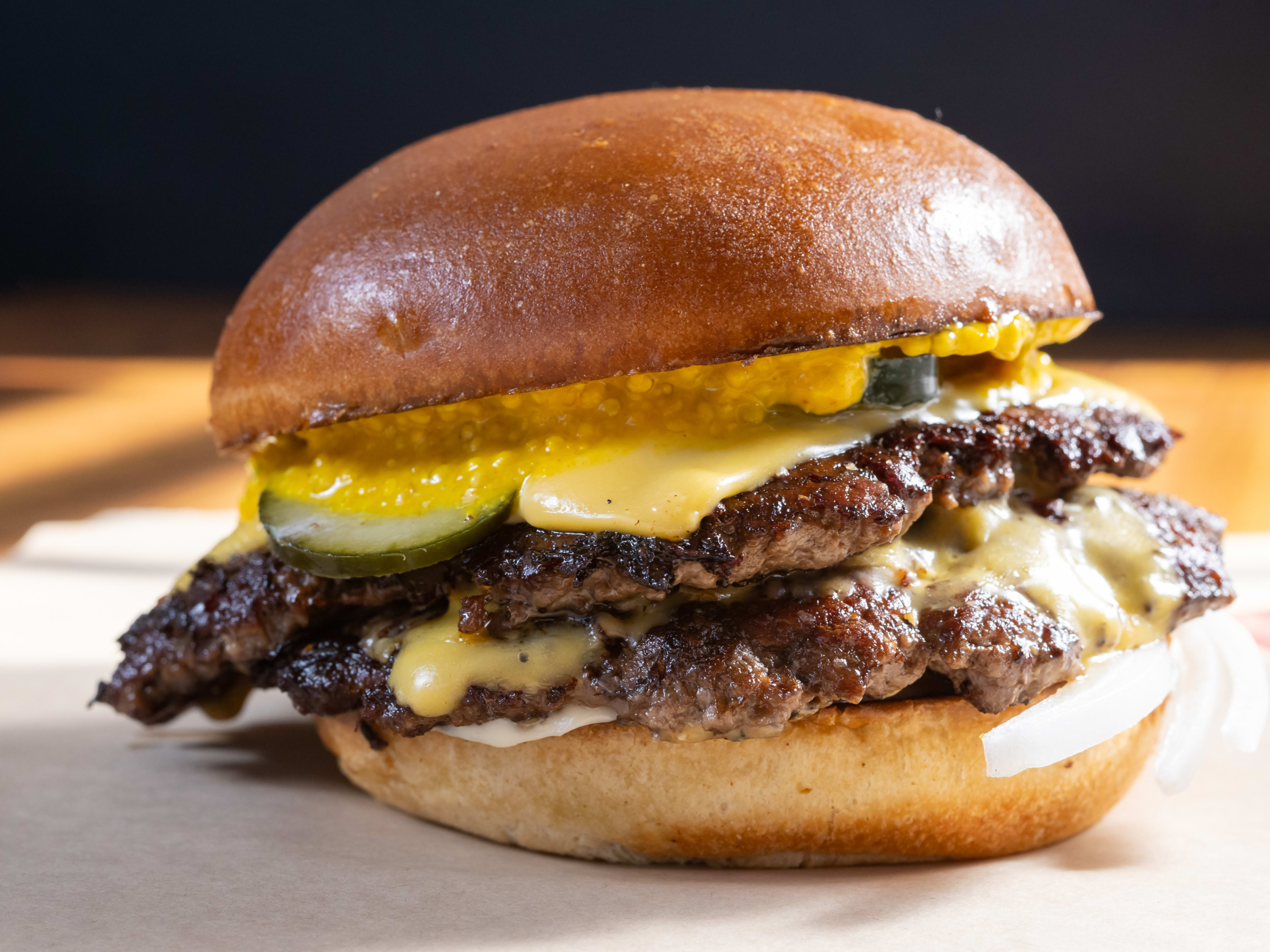 Double-stacked smashburger with yellow mustard, bread and butter pickles, american cheese, and raw onion on a toasted bun.