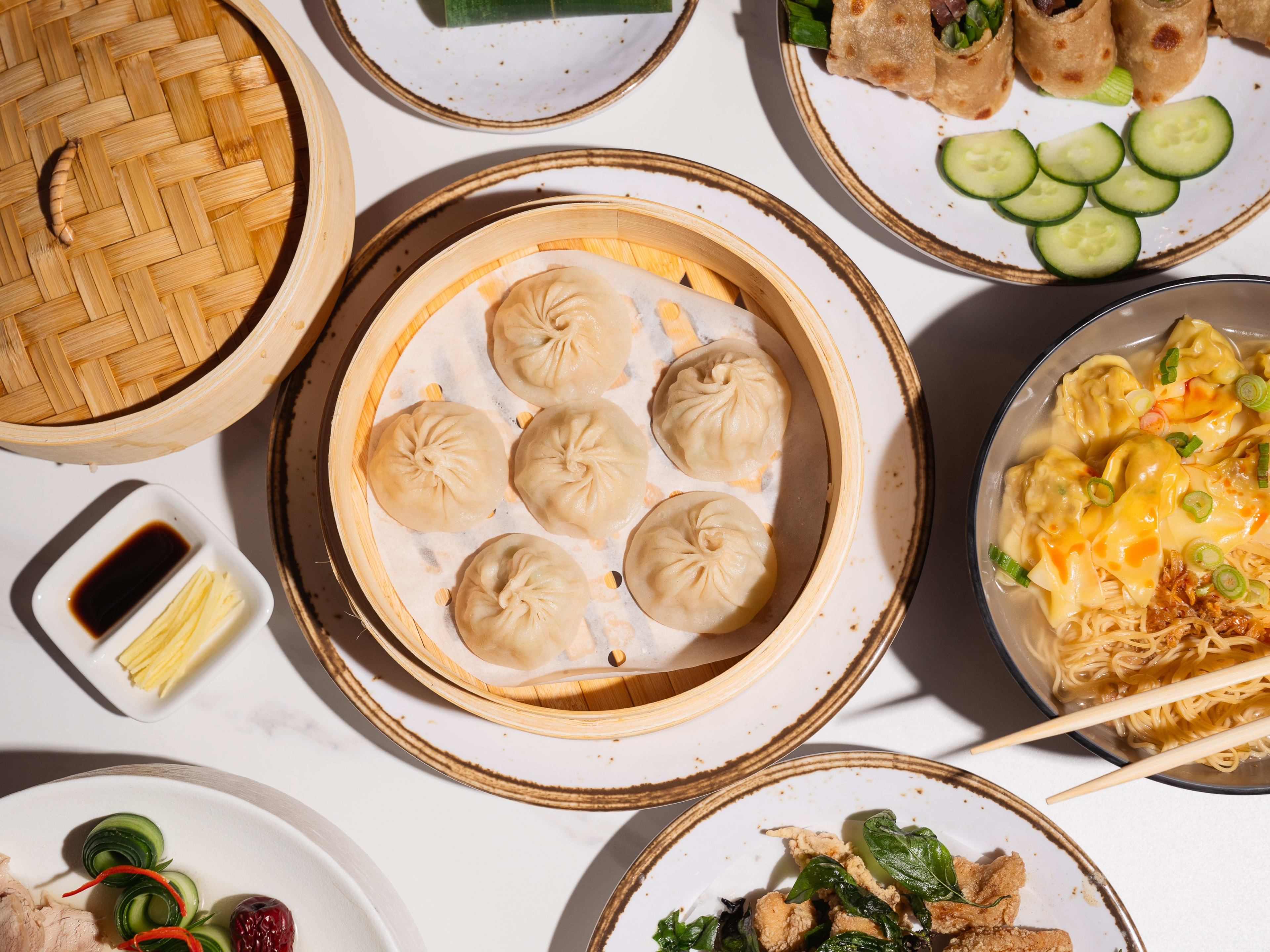 A spread of dishes with plates full of soup dumplings and noodles.