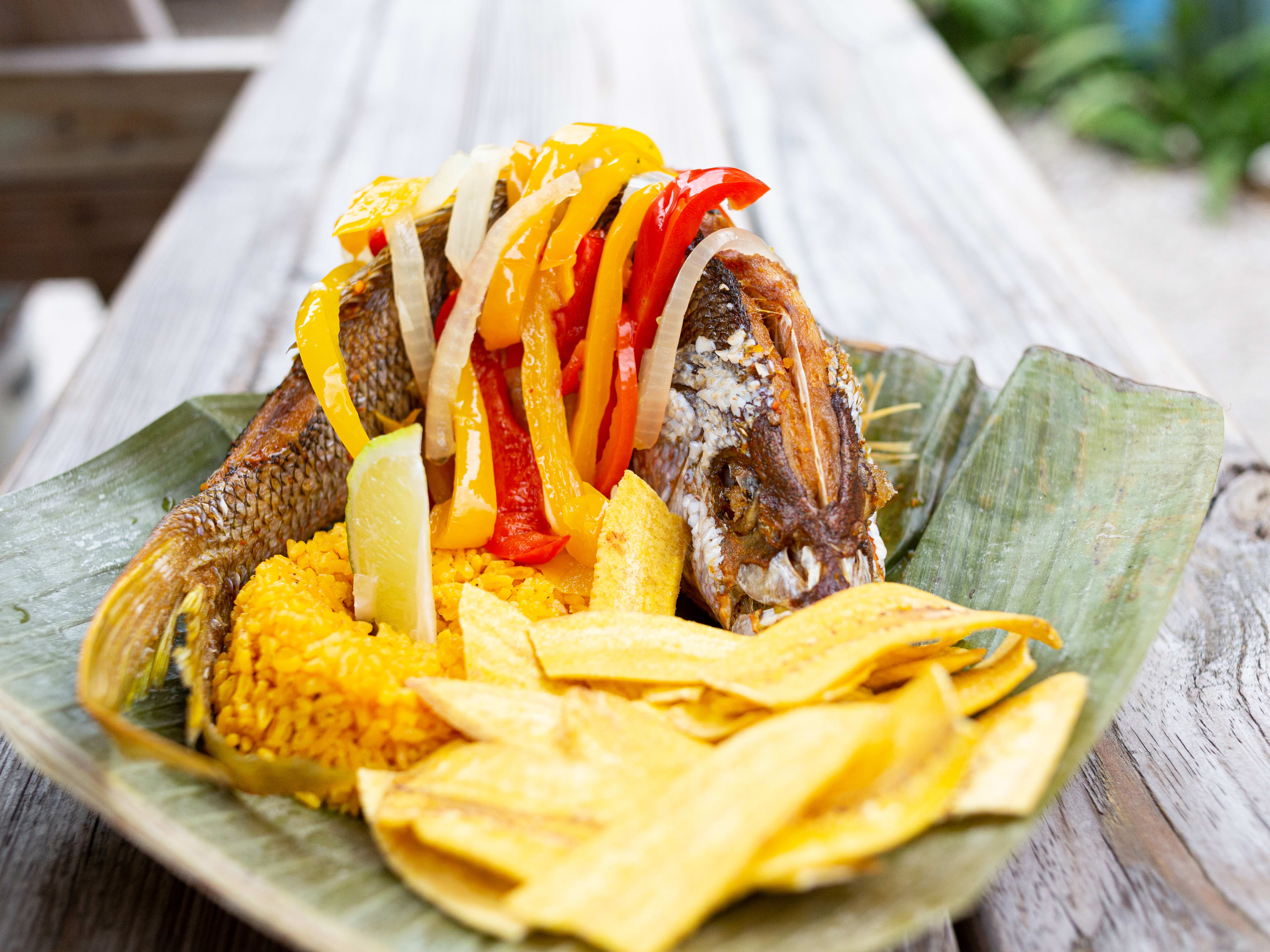 whole fried fish with rice and plantains on a leaf lined plate