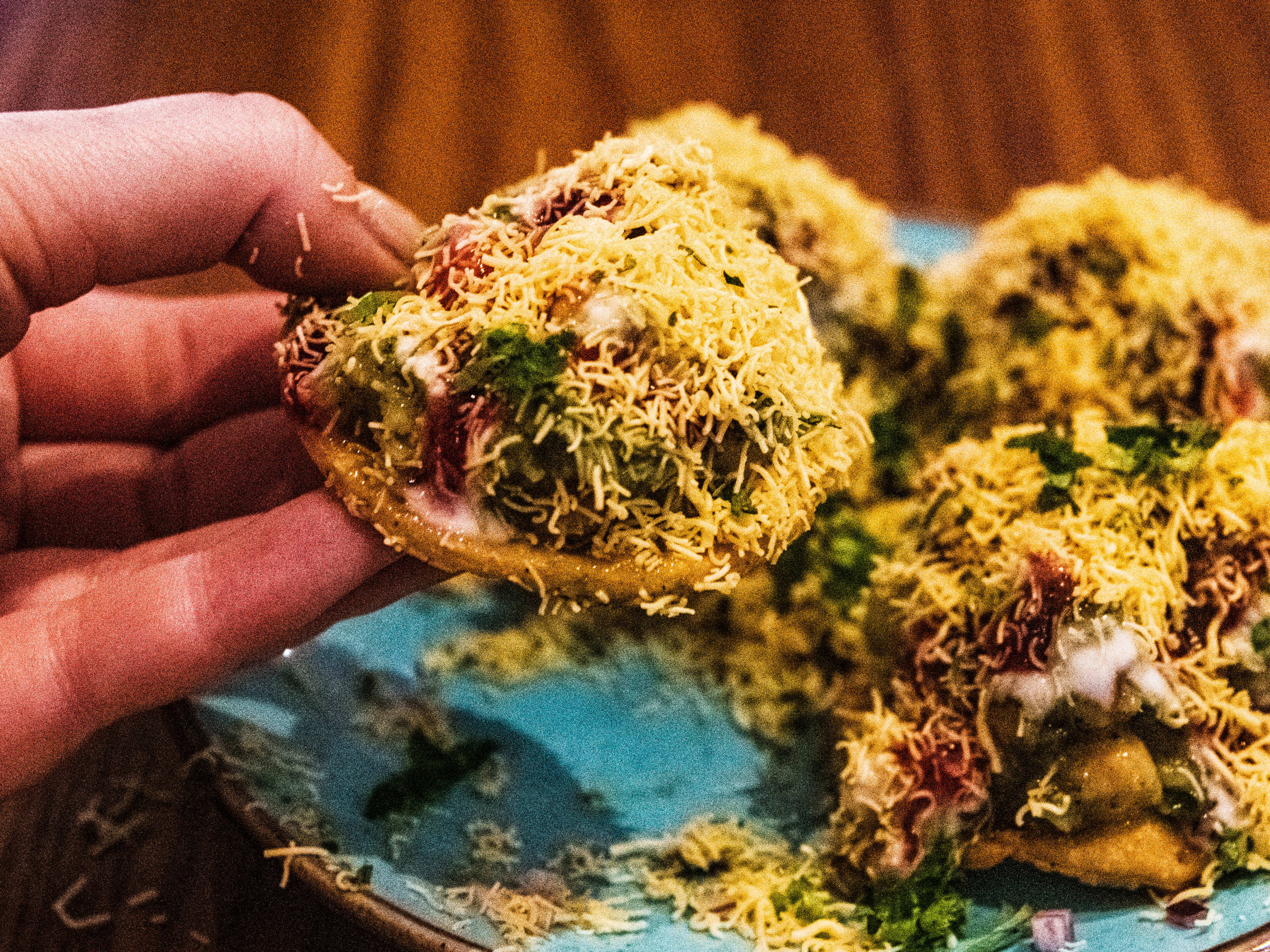 A person lifts up an aloo papdi chaat from a plate.