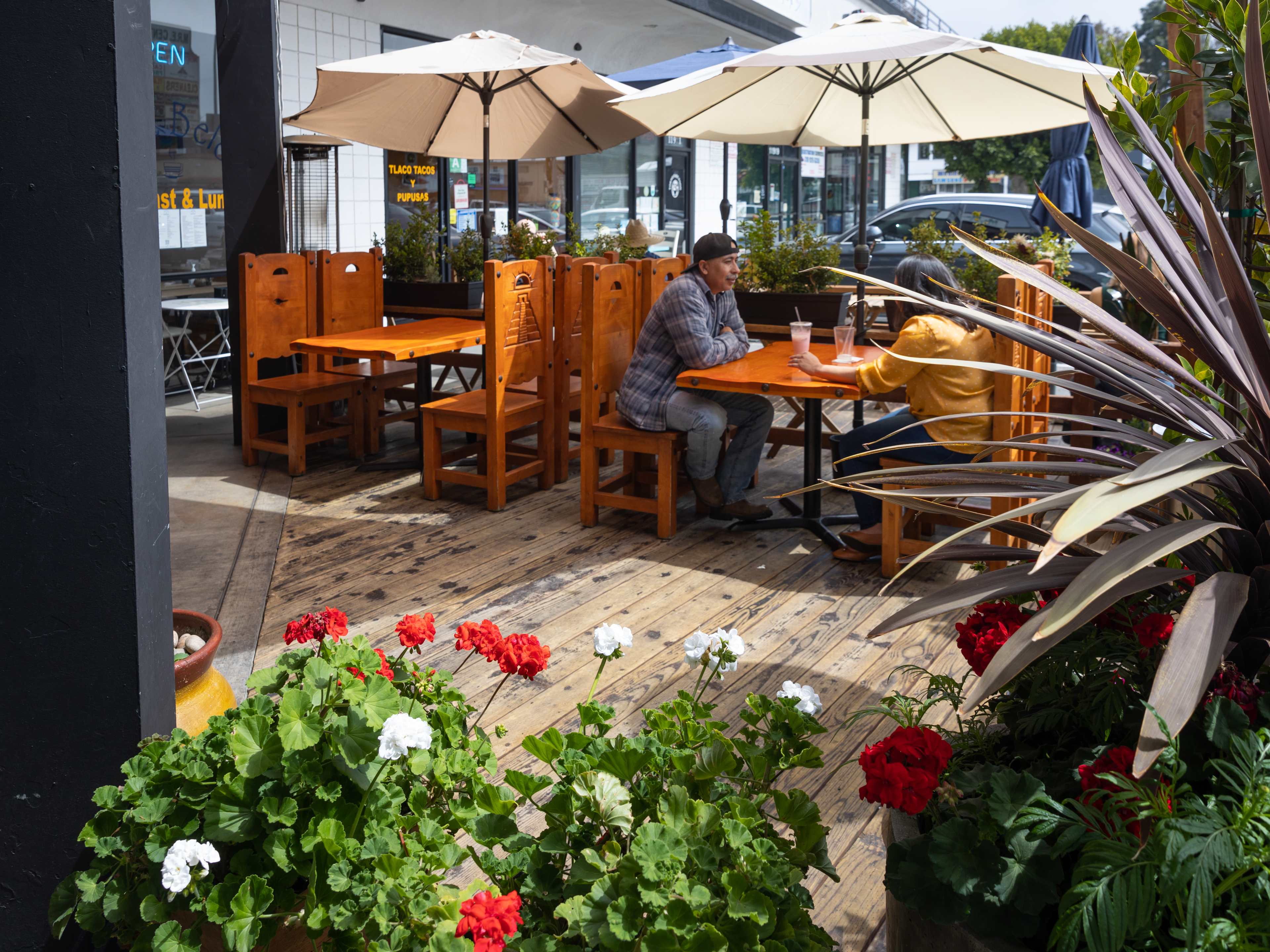 People dining at an outdoor table at Monte Alban. There are plants and flowers.