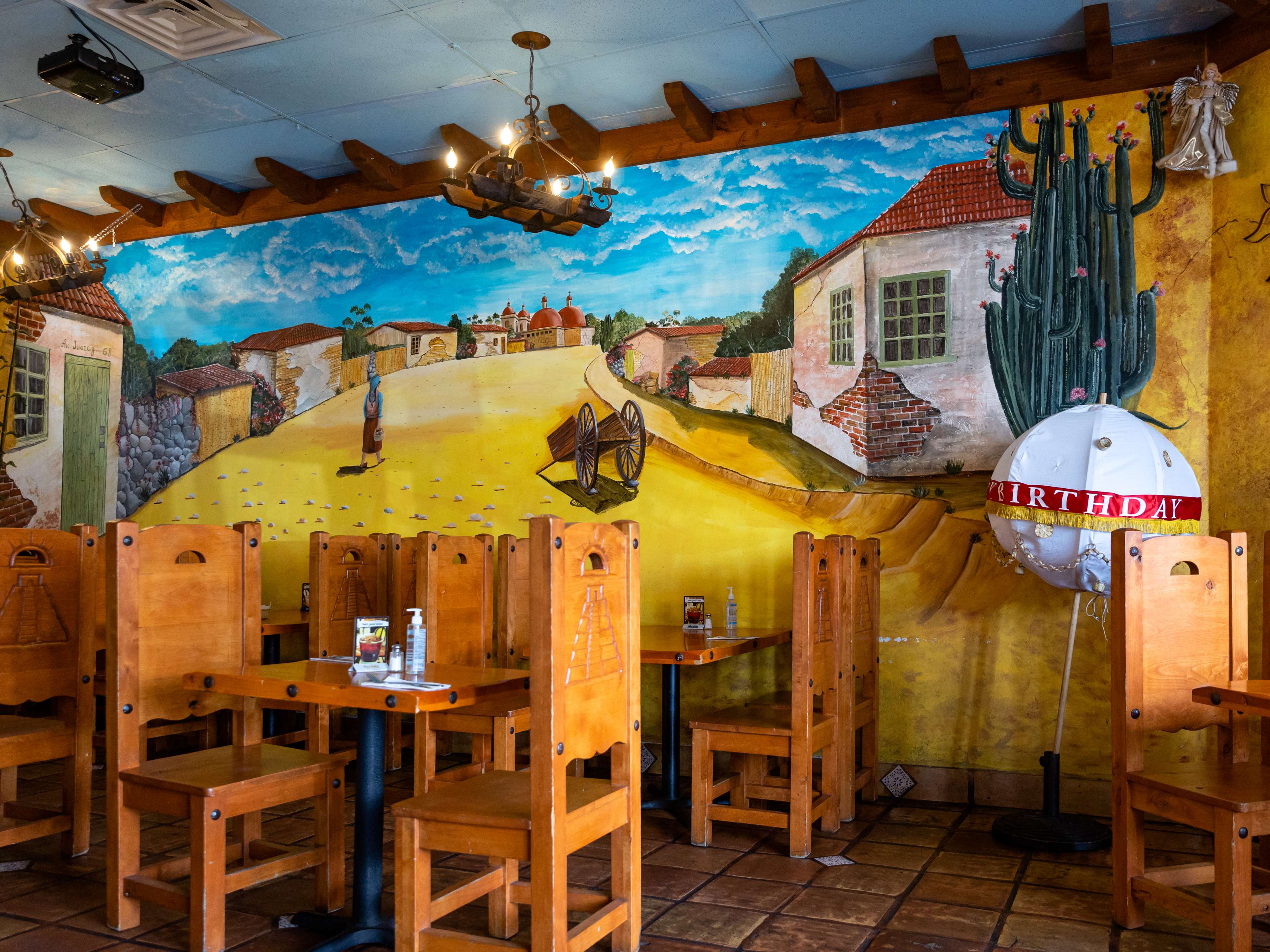 The interior of Monte Alban. A countryside mural is painted on the wall and the tables and chairs are wooden.