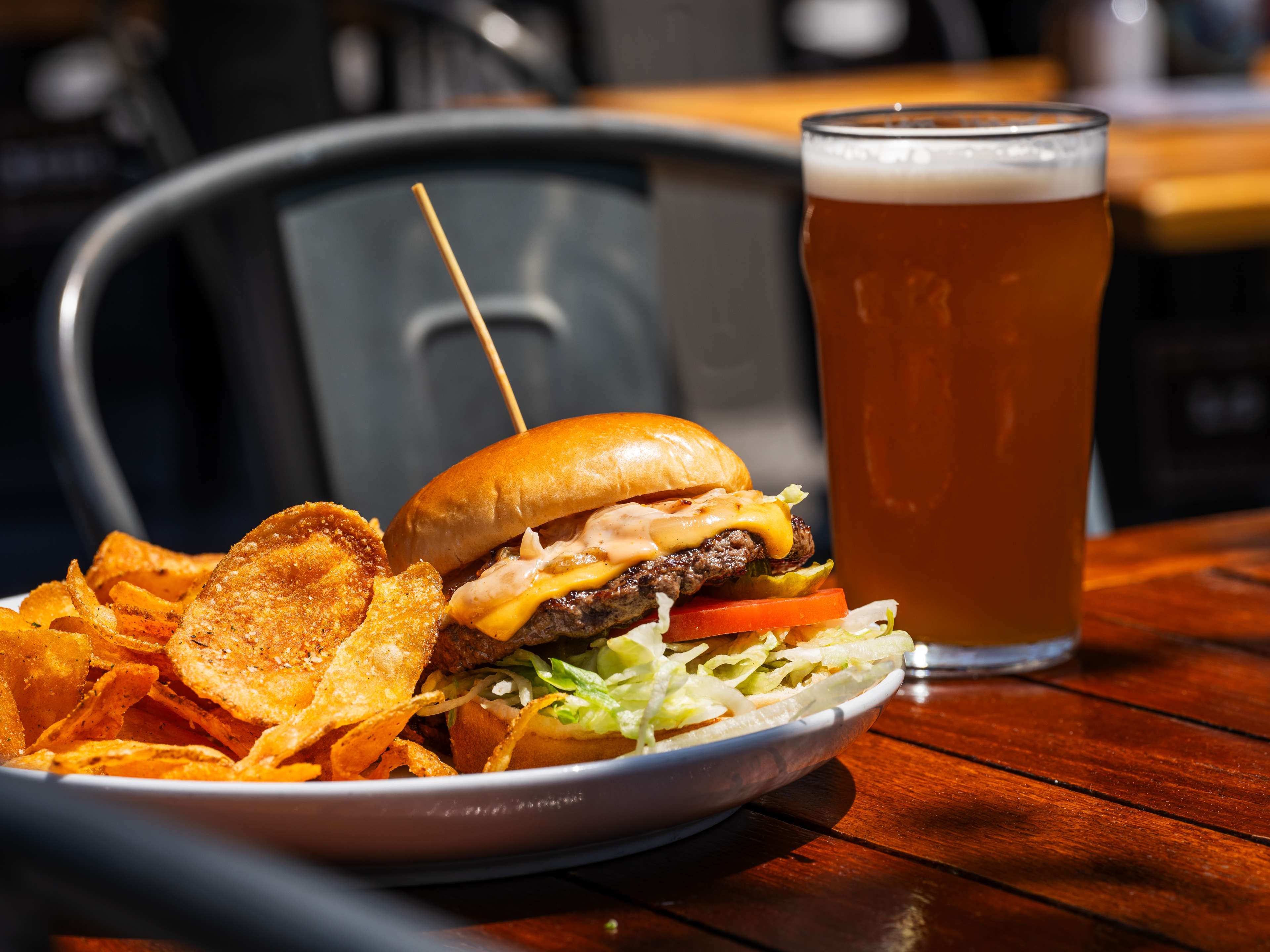 burger and potato chips next to glass of beer on outdoor table