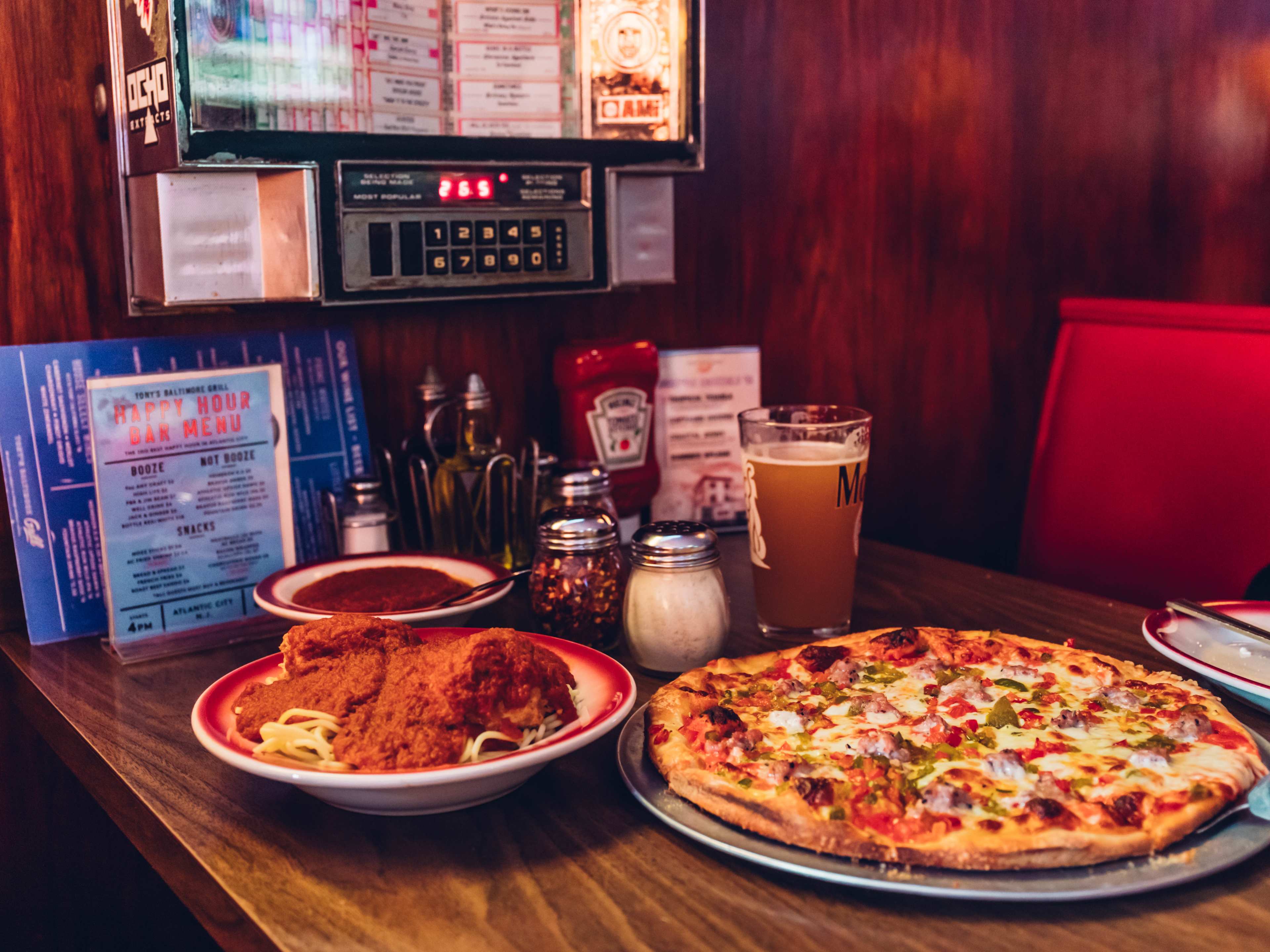 Spaghetti and meatballs and pizza in a red booth with a booth jukebox selector.