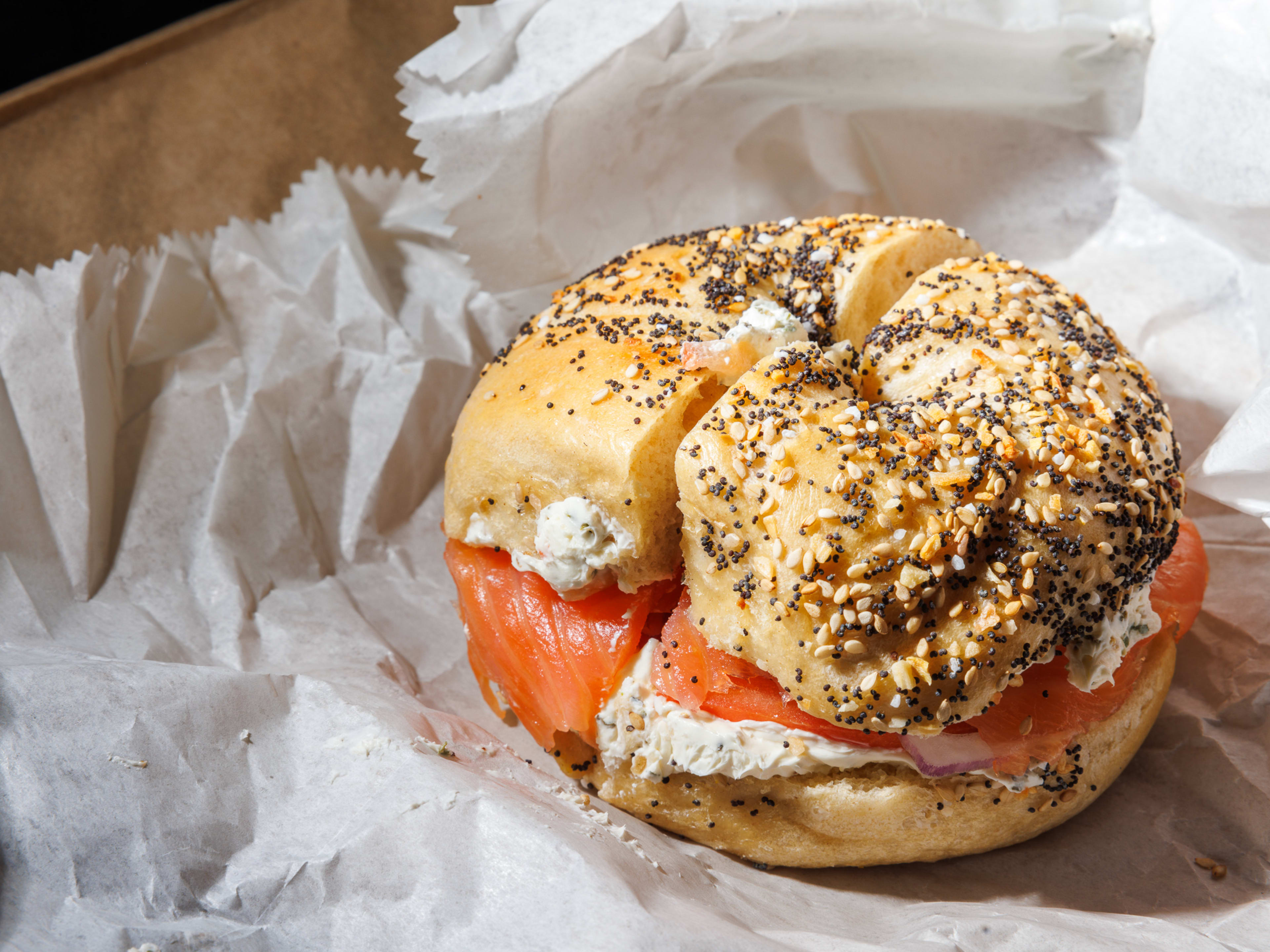 An everything bagel with cream cheese and lox on white paper.