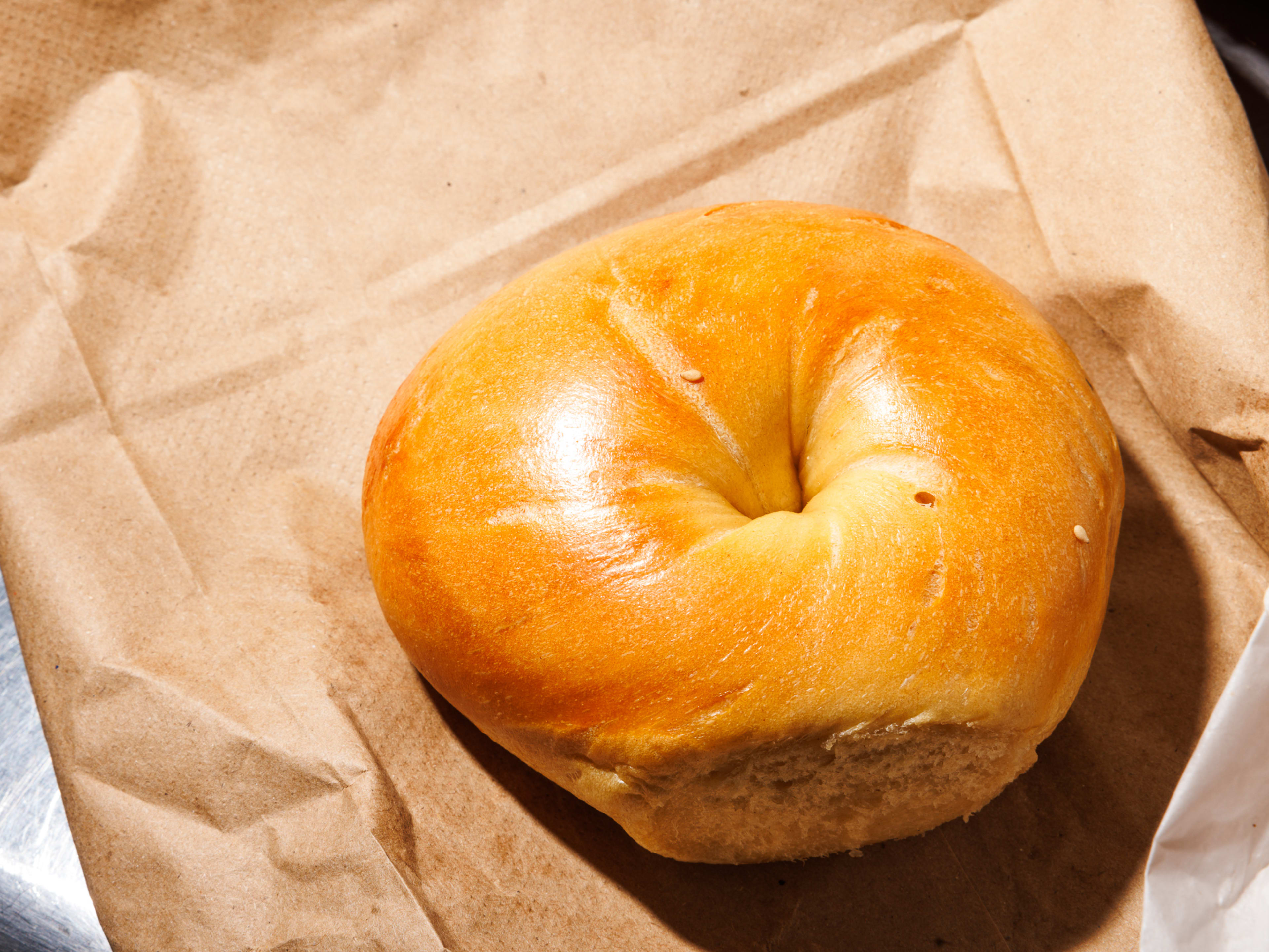 A plain bagel on a brown bag.