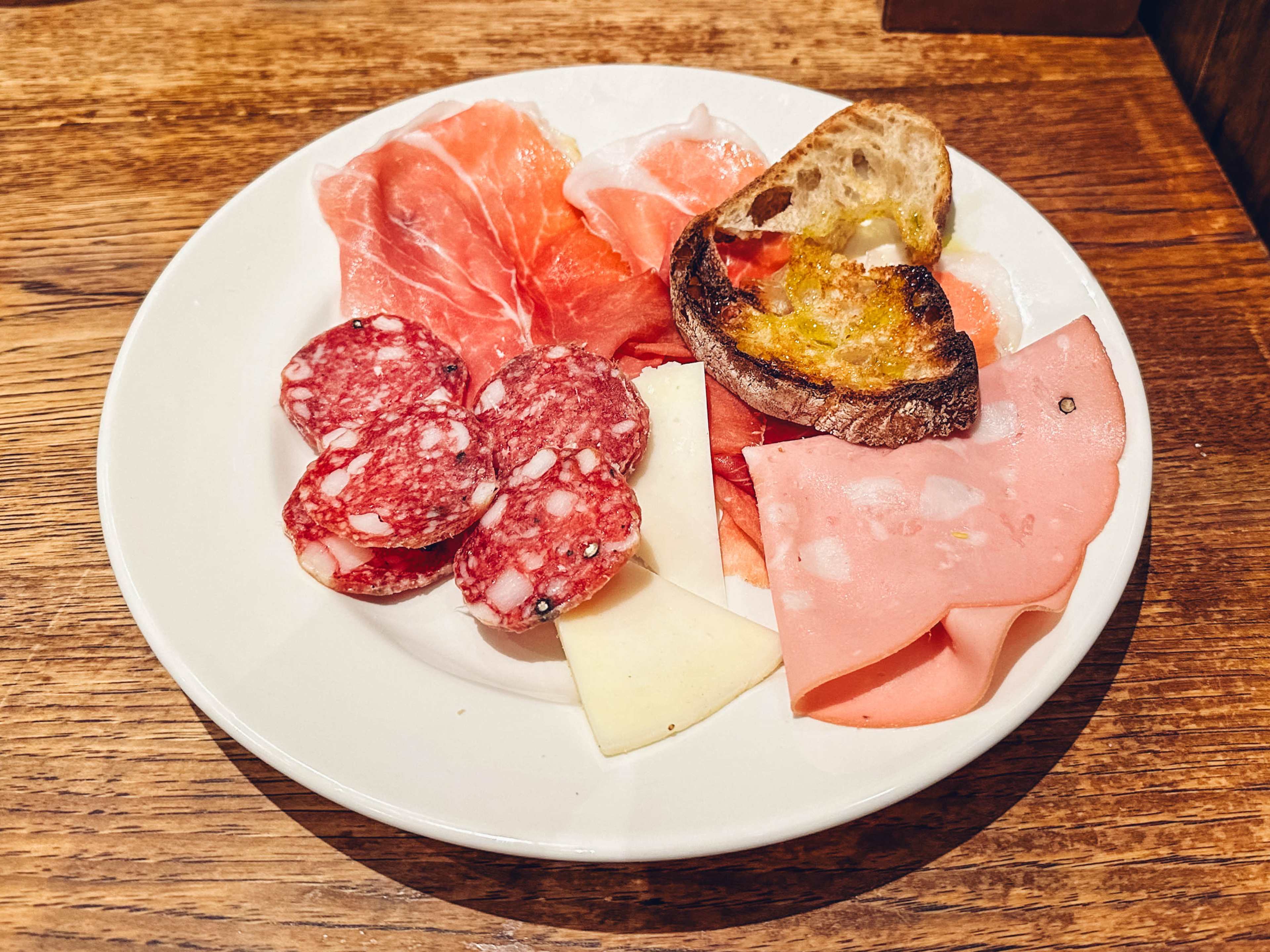 A platter of cured meats with a slice of toasted bread.