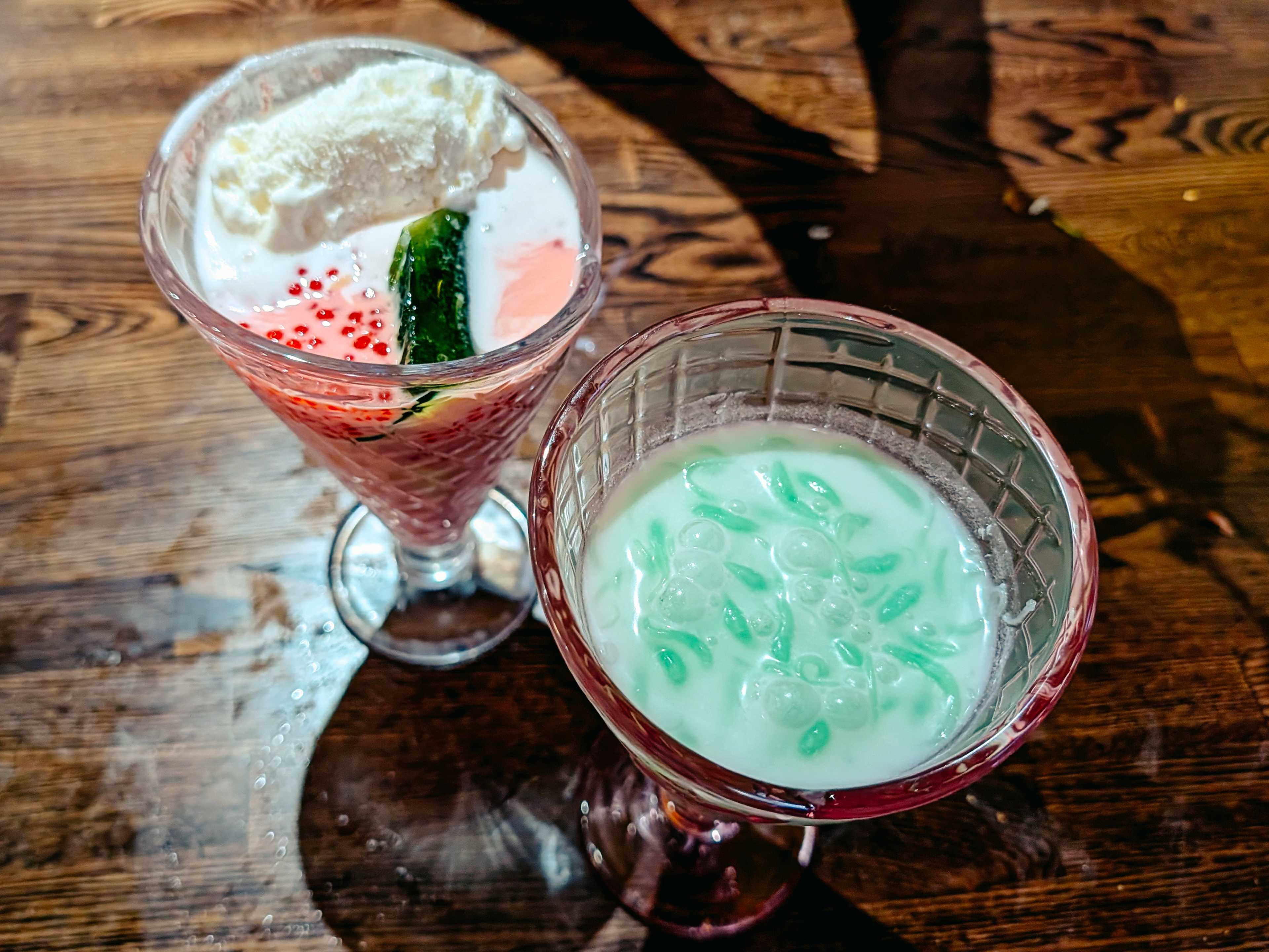 two colorful desserts in goblets; one is white with red bead-like things in it, and the other is green