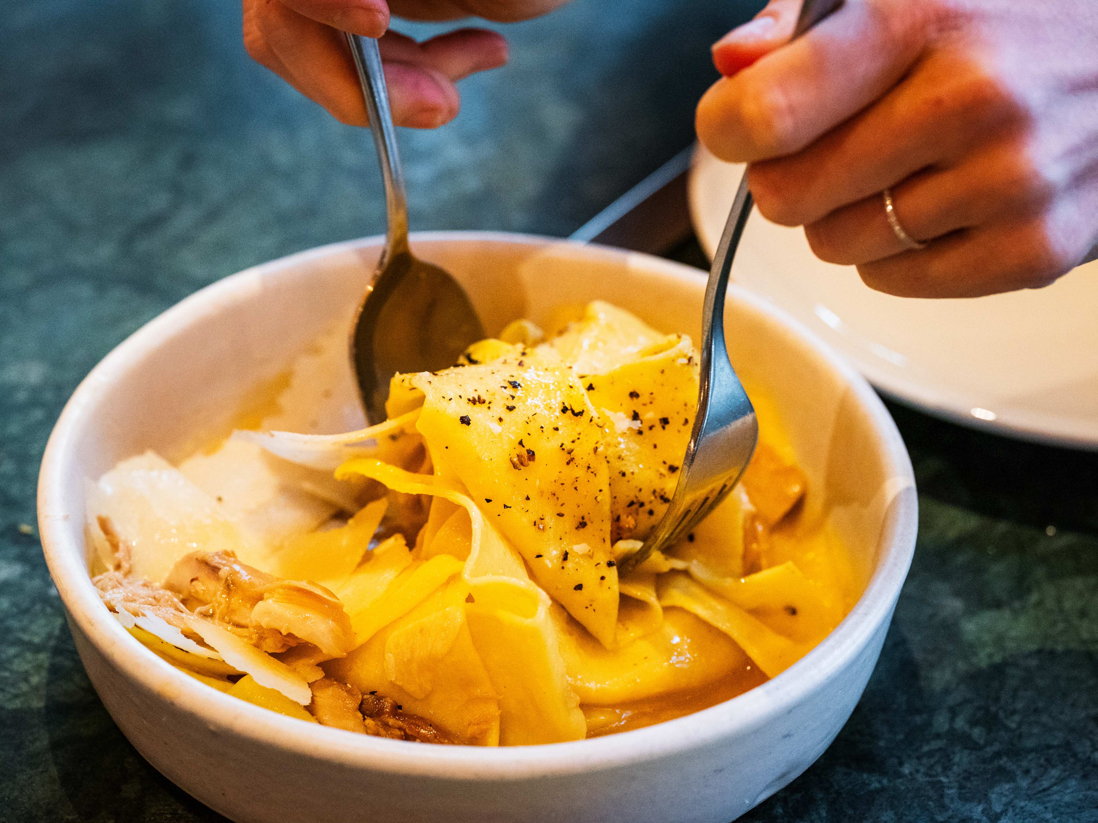 tossing the stracci pasta in a white bowl.