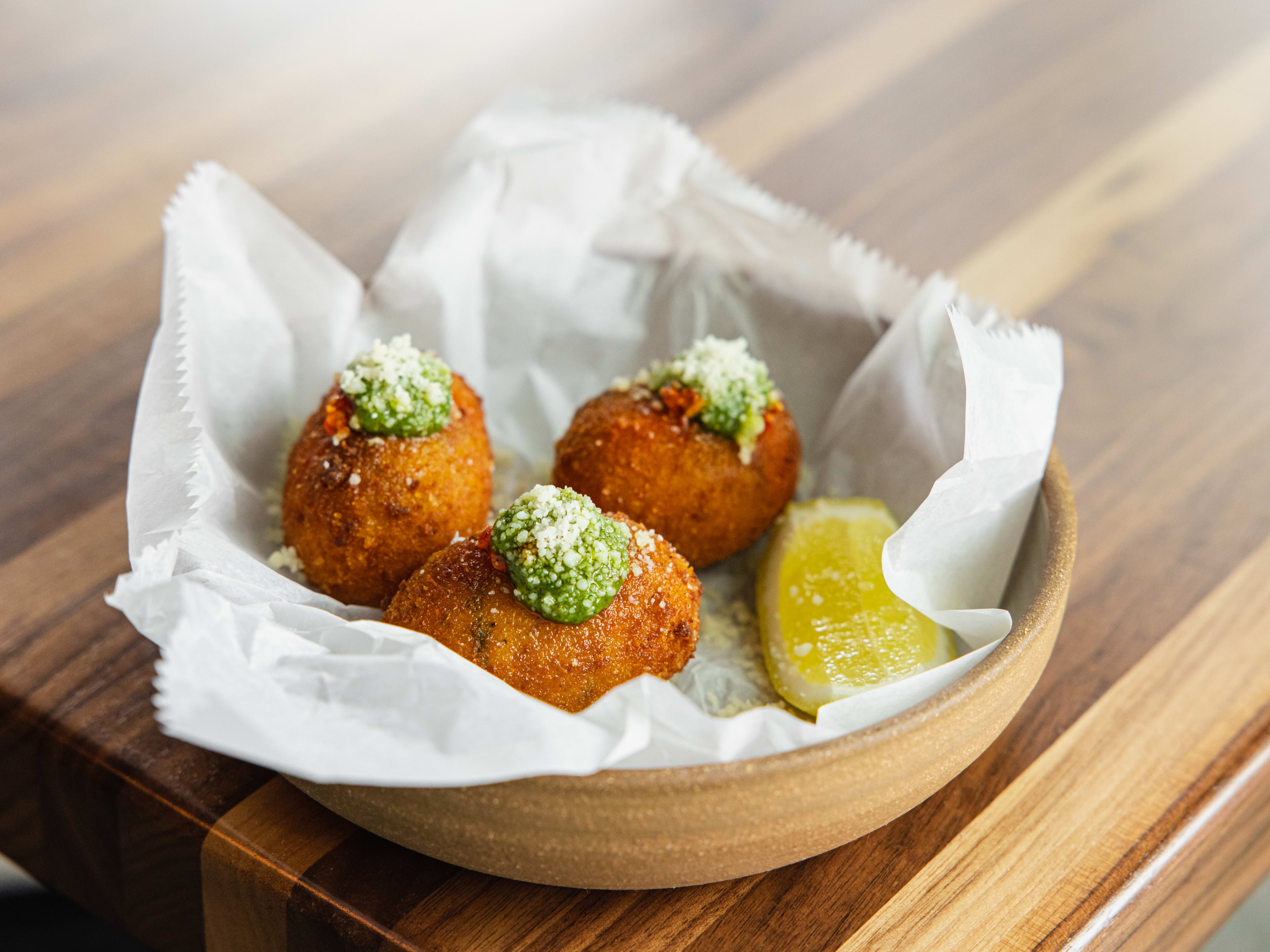 A bowl of arancini with a lemon wedge on the side.