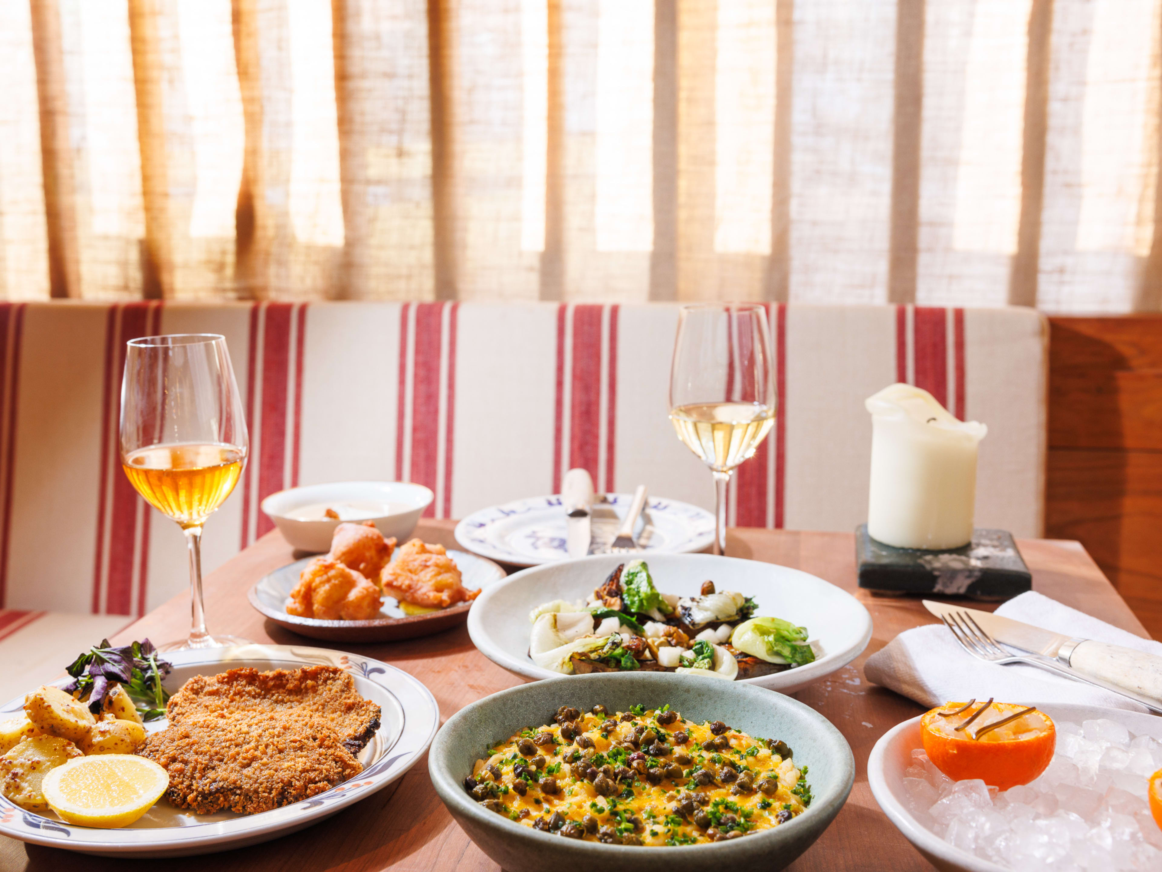 A spread of 6 dishes from Gem Wine, with two glasses of wine and a large, chunky candle.