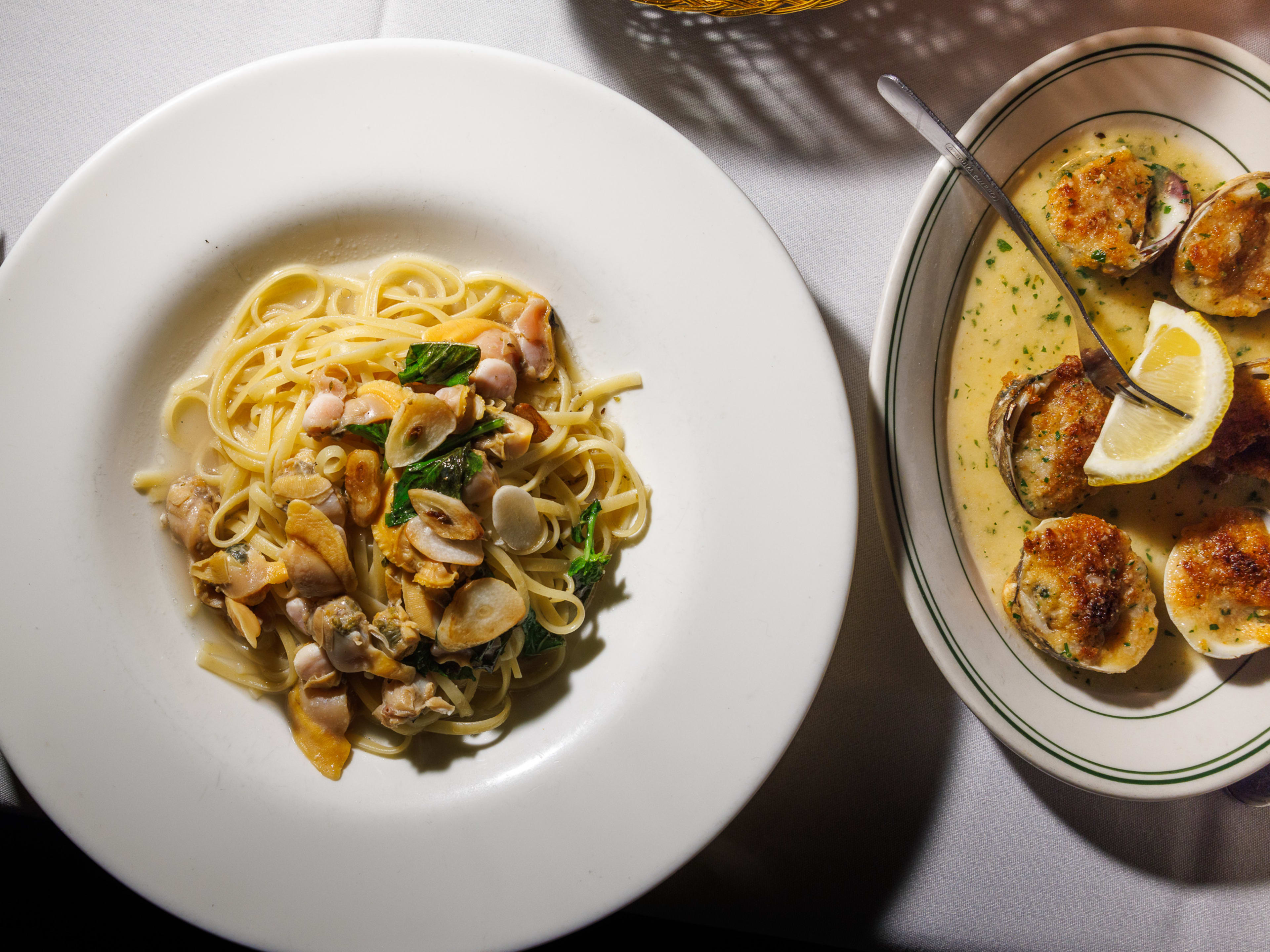 A bowl of linguine with clam sauce and a plate of baked clams.