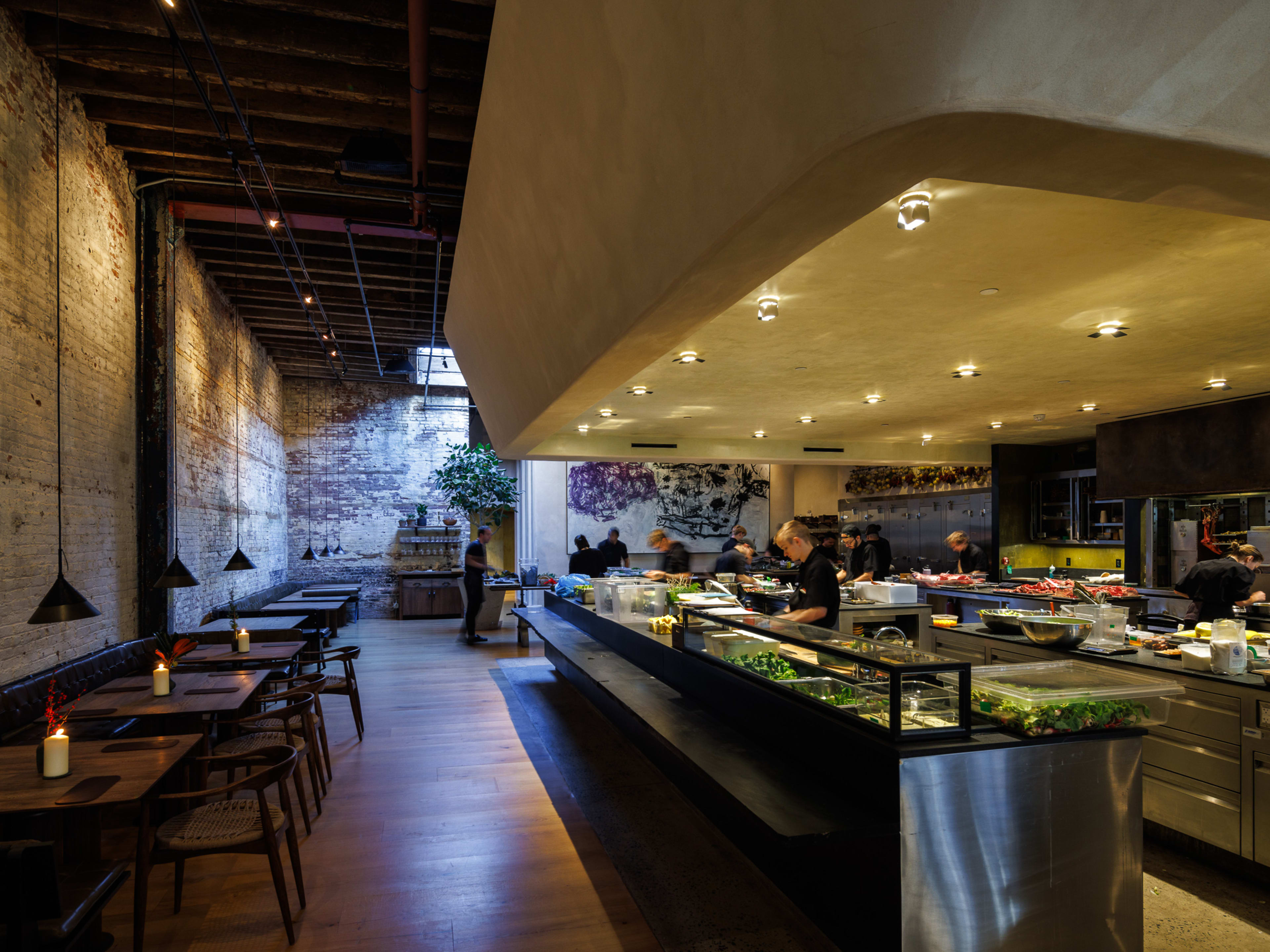 A dining room in a former warehouse with a big open kitchen in the middle.