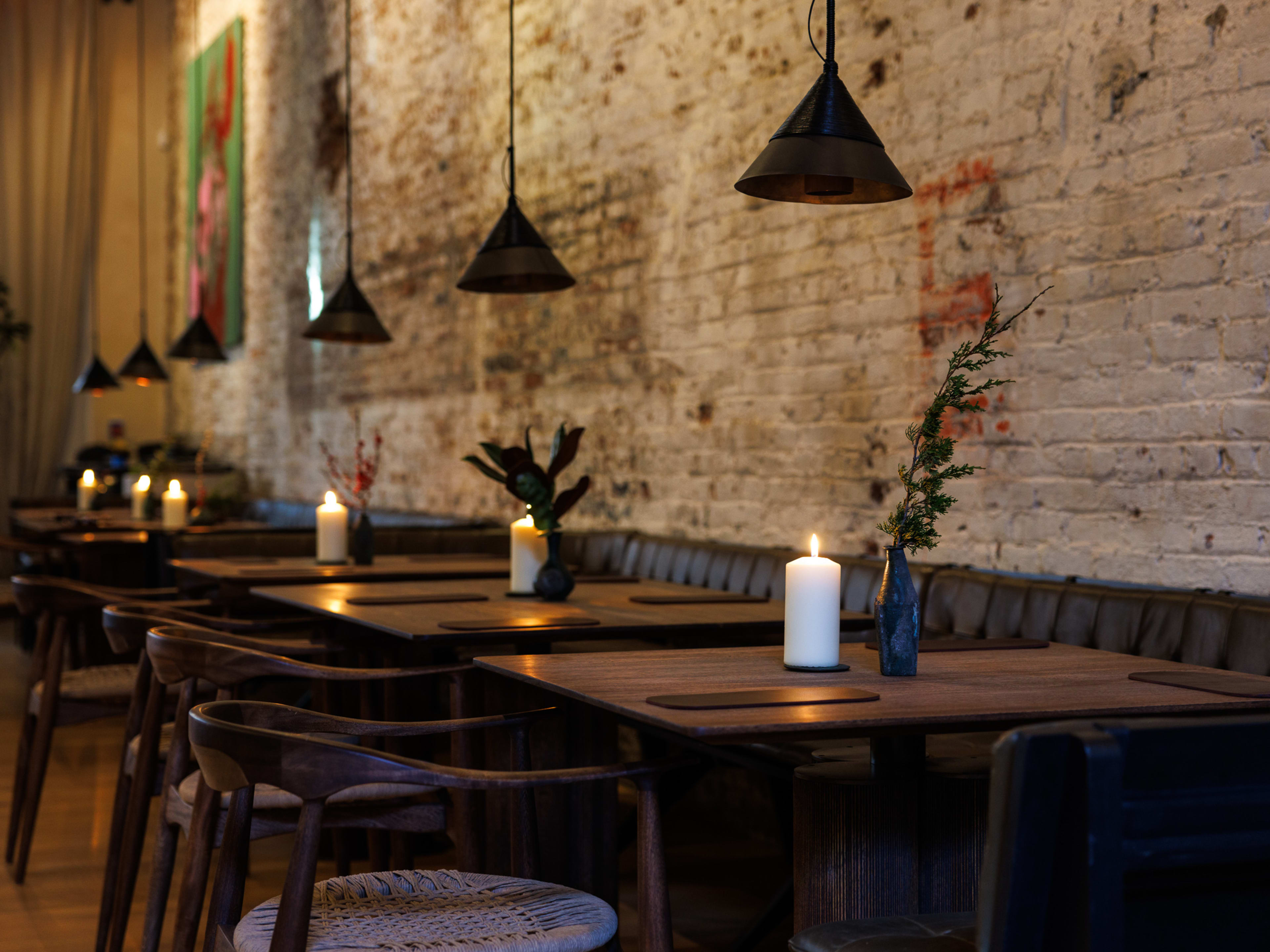 Tables topped with candles in a restaurant with a brick wall behind them.