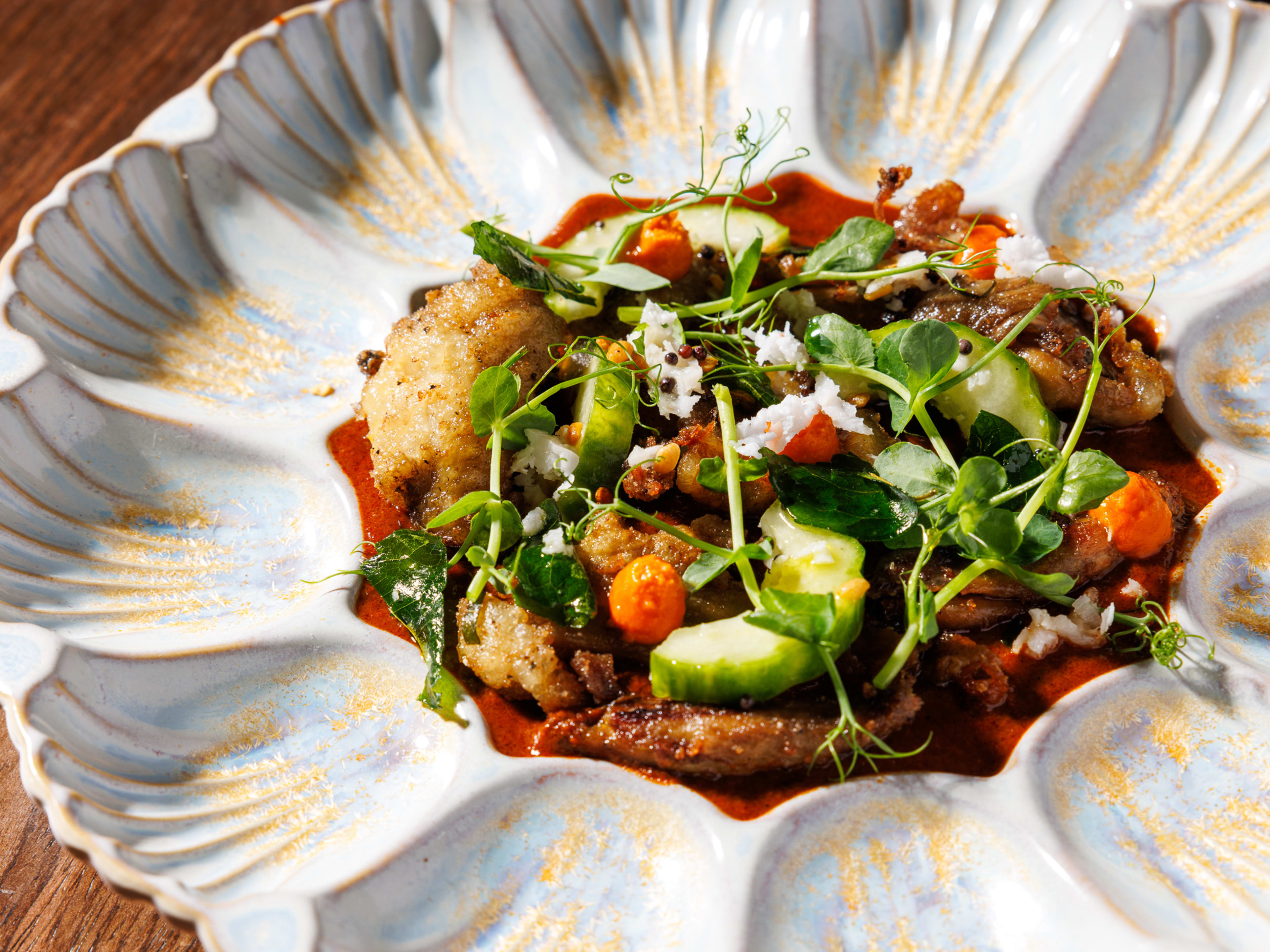 Pieces of roast duck topped with micro greens and cucumber, sitting in a rich red sauce.