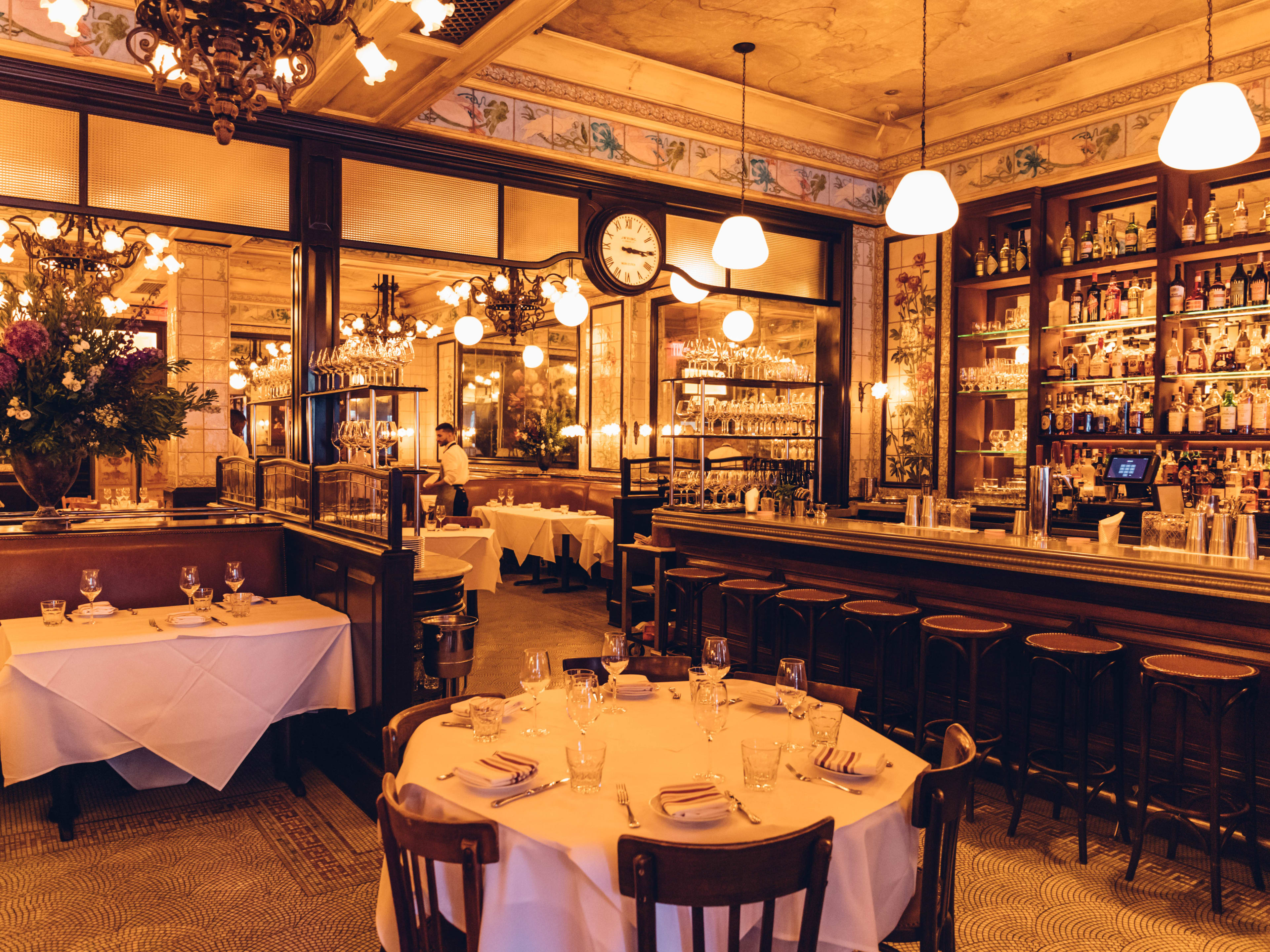 A baroque dining room with soft yellow lighting, white tablecloths, and intricately tiled walls.