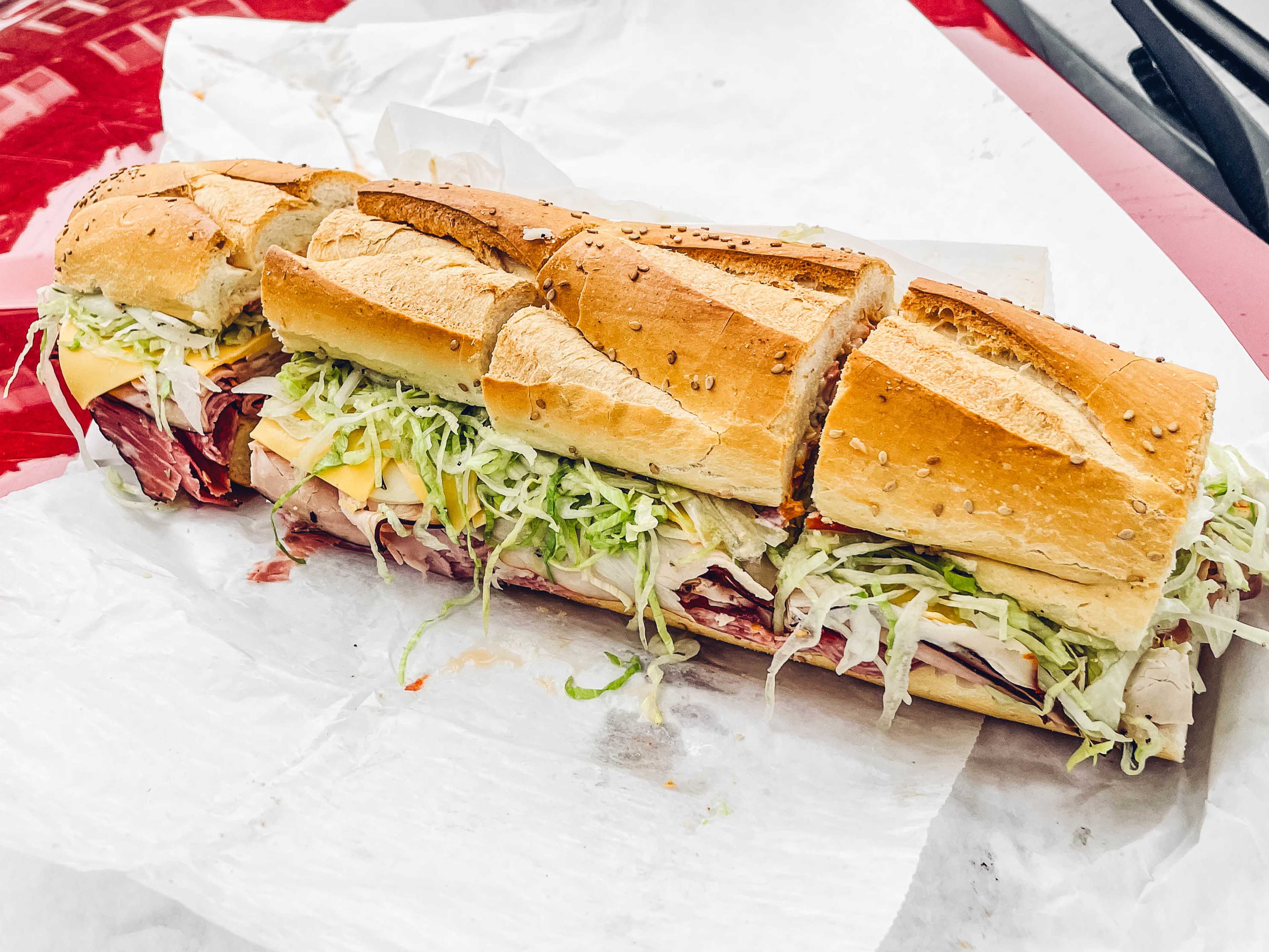 a gigantic cold cut sandwich sitting on the hood of a car