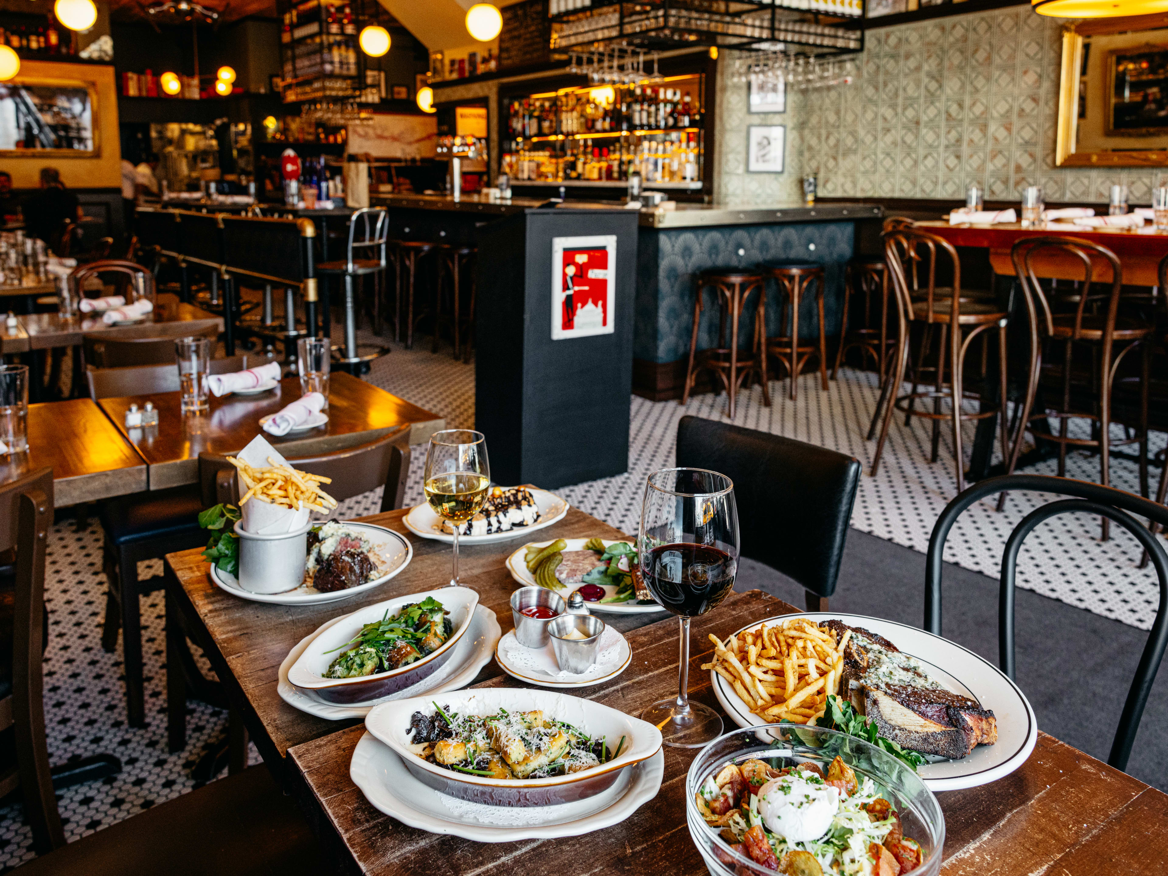 A big bistro table covered with steak, fries, salad, and wine.