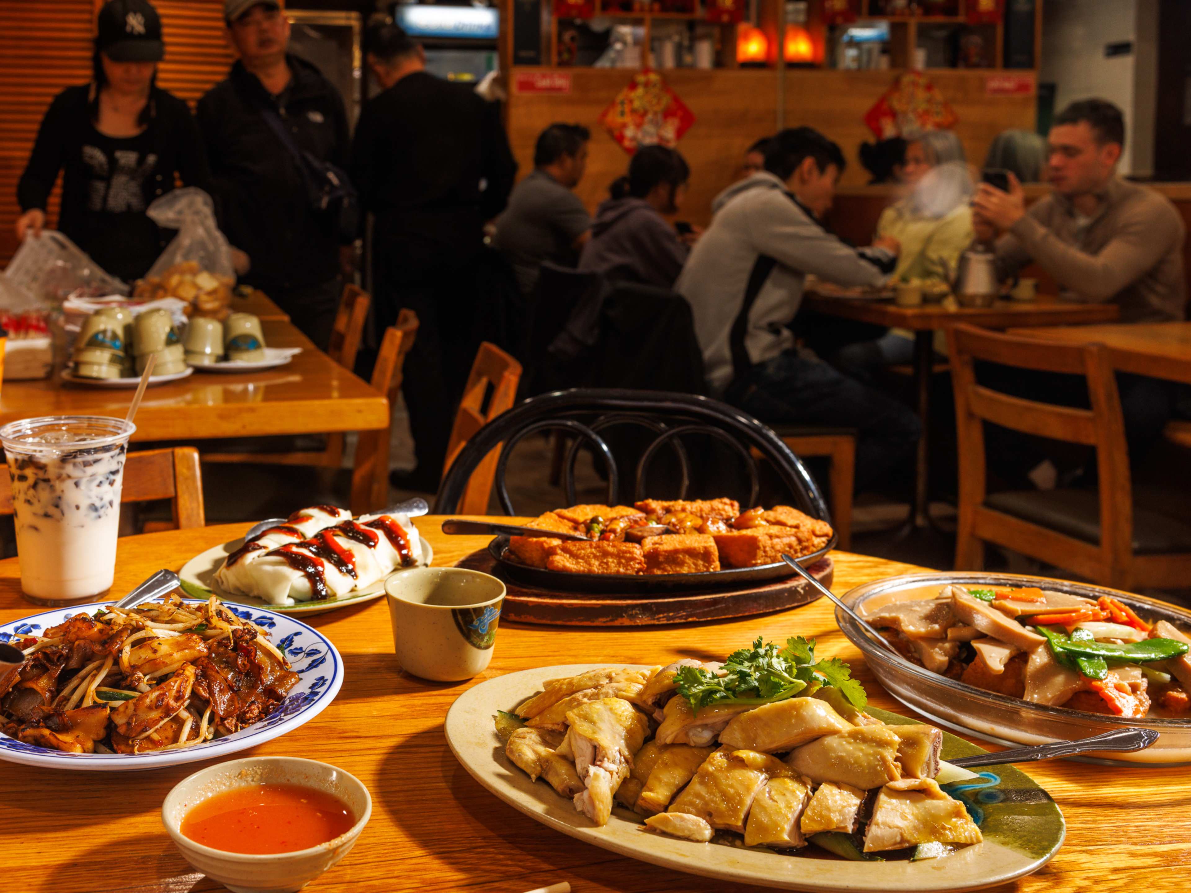 A spread of dishes on a table with people eating in the background at Taste Good Malaysian.