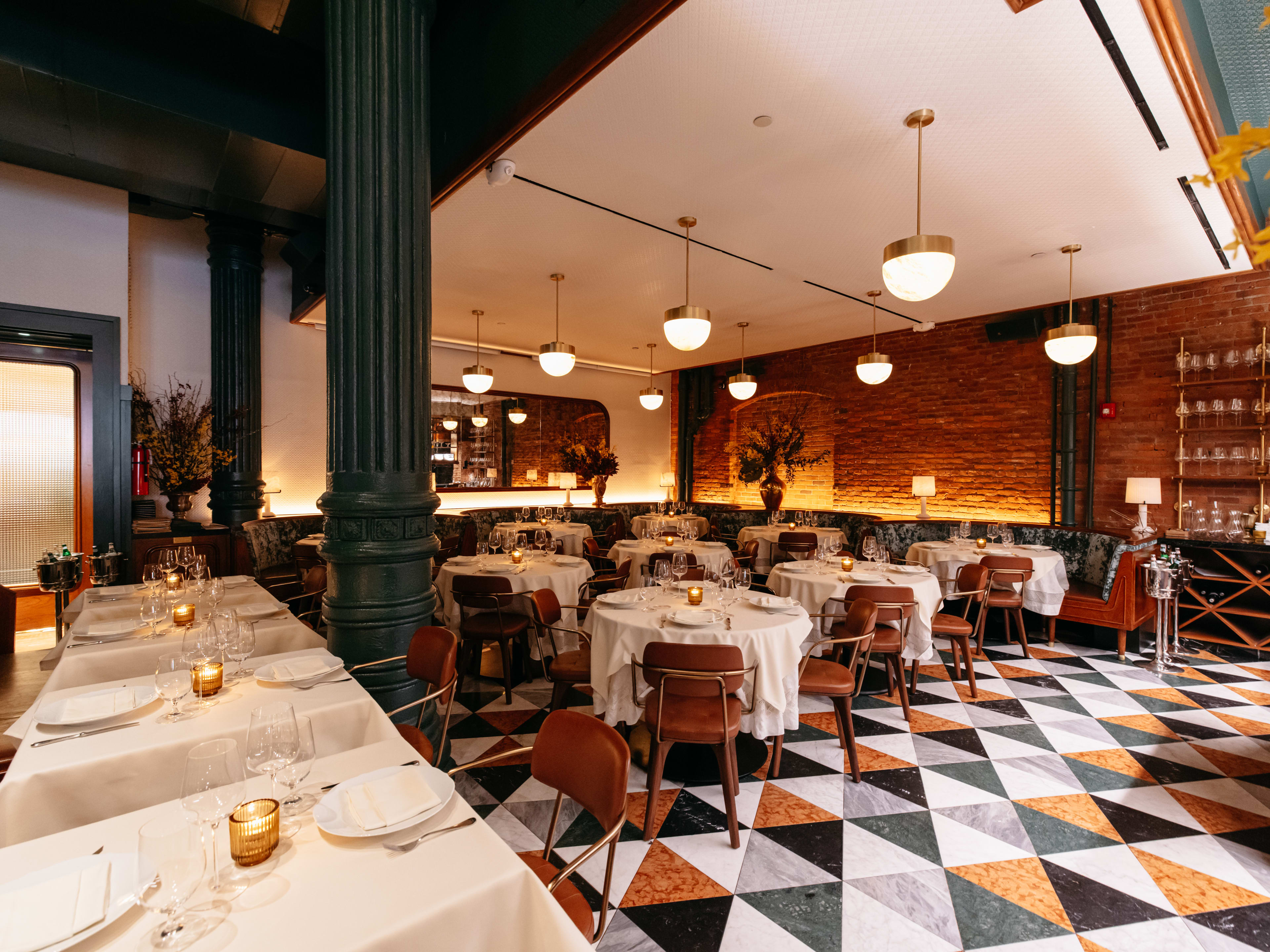 A fancy dining room with hanging lamps, green columns, and white tablecloths.