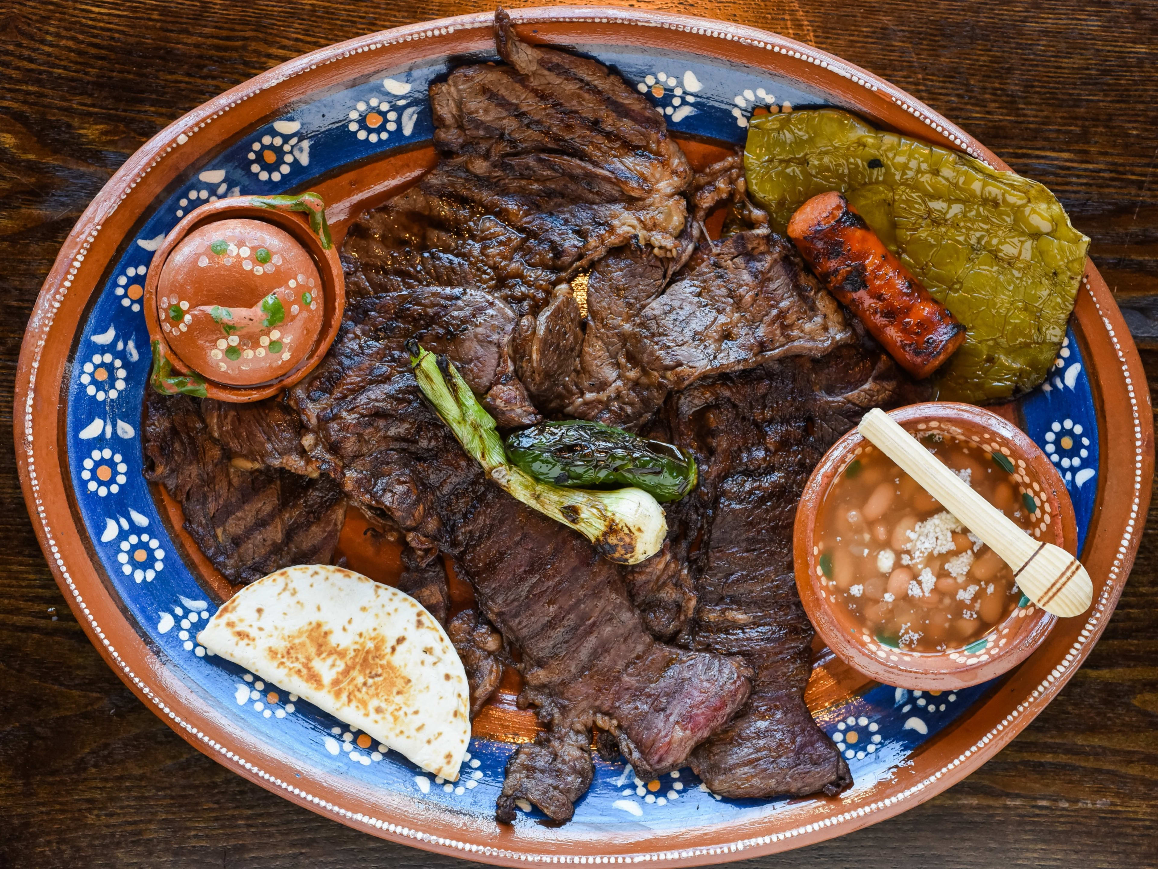 Plate of carne asada with a side of beans, cactus, and a mini quesadilla